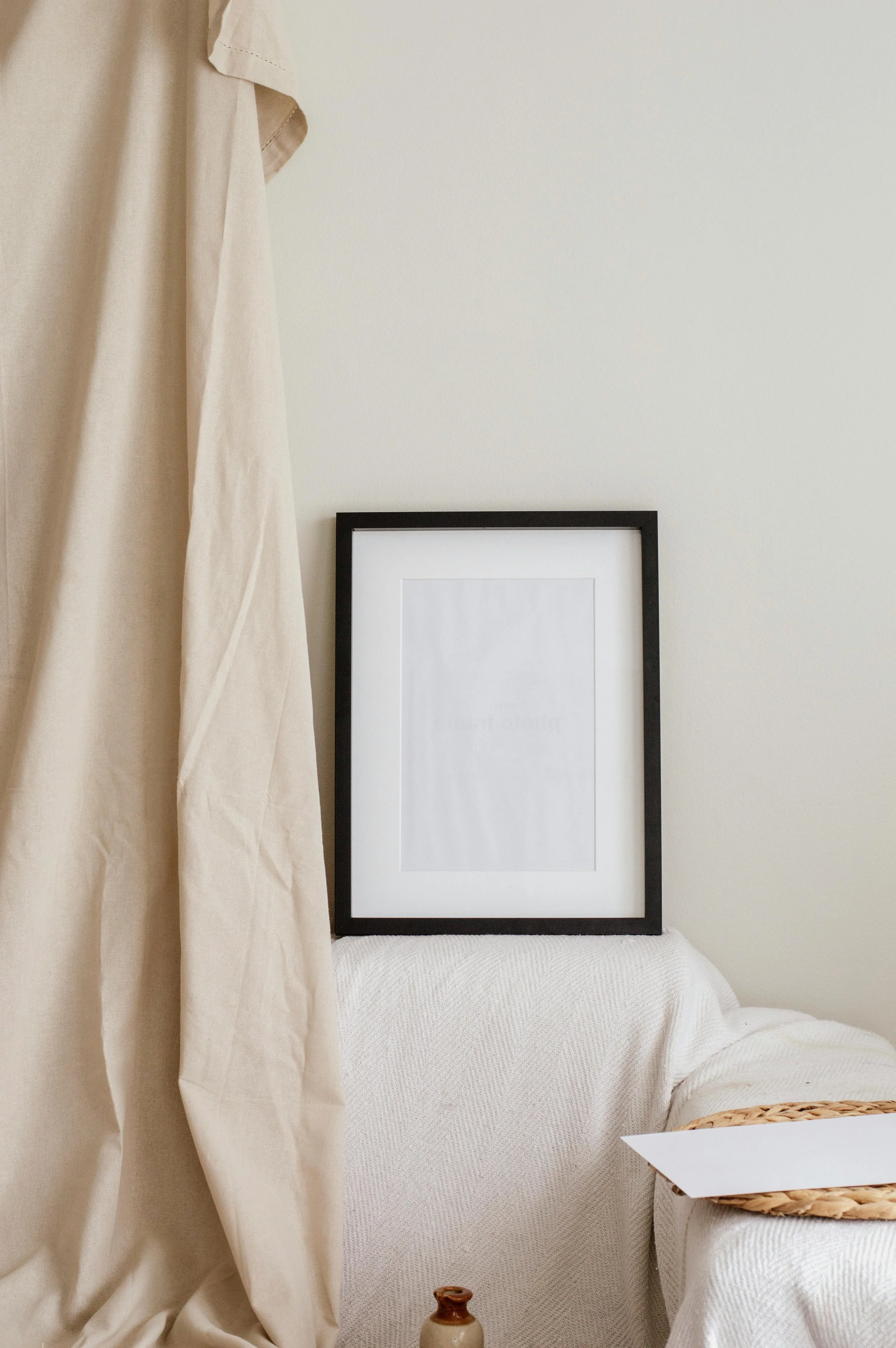 Empty black picture frame resting on a white textured sofa next to a beige curtain.