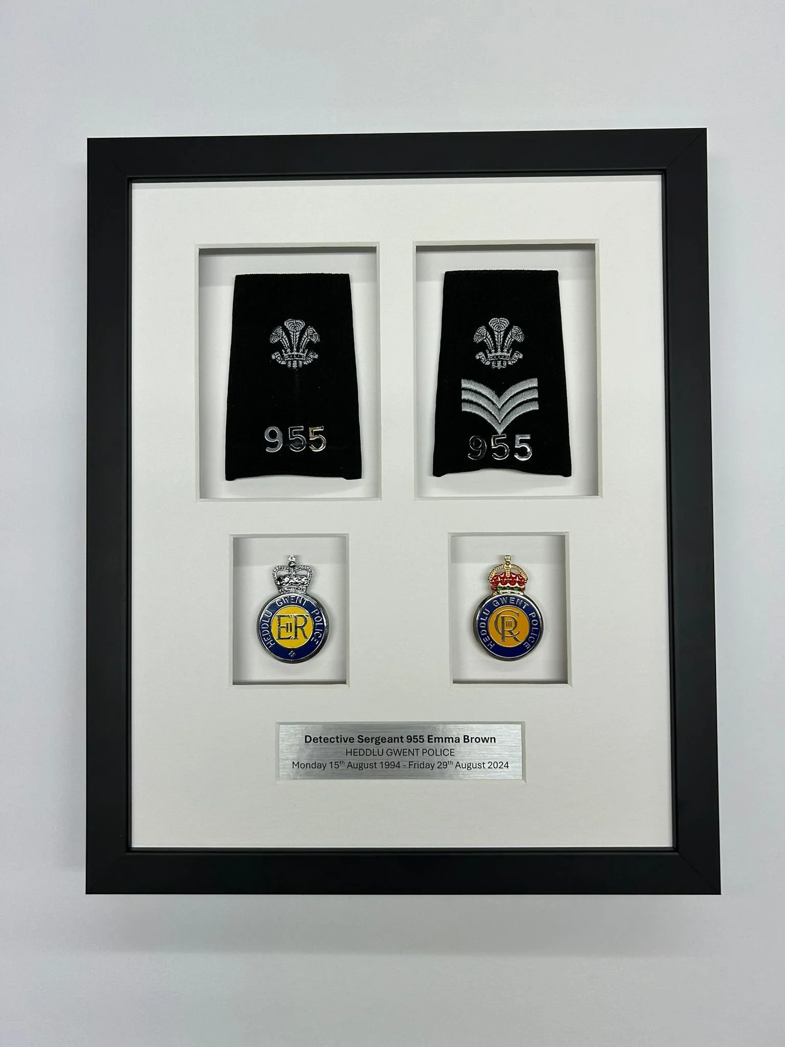 A framed display featuring police insignia, badges, and a nameplate for Detective Sergeant Emma Brown, who served from August 15, 1994, to August 29, 2024, including two shoulder patches and embroidered insignia with the number 955.