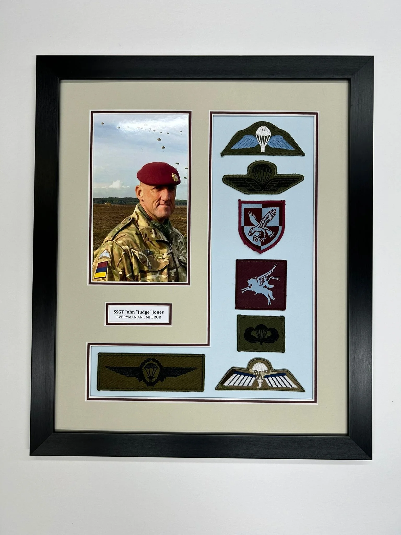 Framed military display with a photograph of SSGT John Jones in camouflage uniform and maroon beret, military patches, and a plaque that reads 'SSGT John 'Judge' Jones. Everyman an Emperor', along with various military patches and badge insignias.