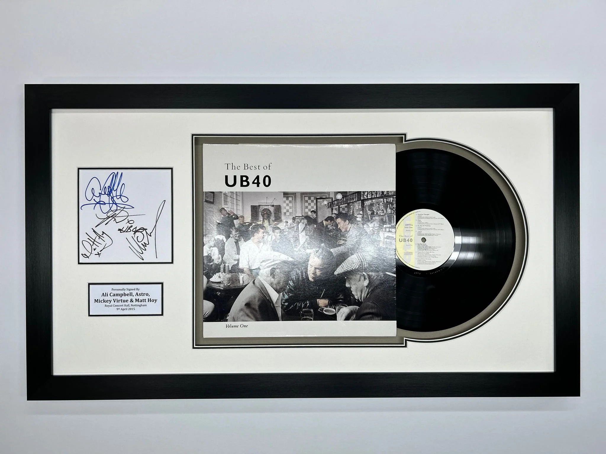 Framed platinum record award for UB40's album 'The Best of UB40', with a black vinyl record on the right and a black-and-white group photo in the center, signed by band members with autographs and a plaque indicating signatures of Ali Campbell, Astro