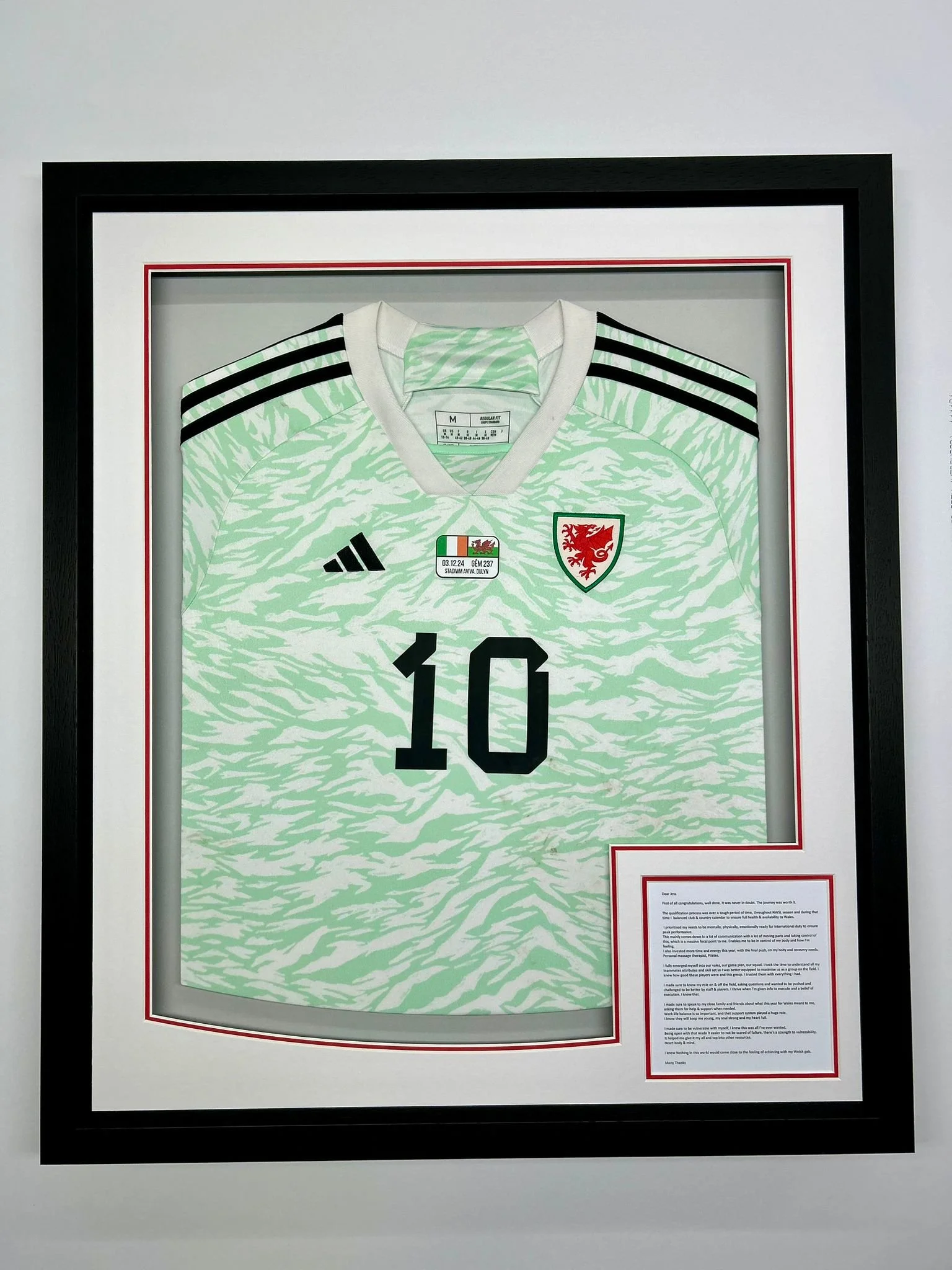 Framed soccer jersey with the number 10, green and white tiger-stripe pattern, black stripes on shoulders, and the Welsh Football Association crest.