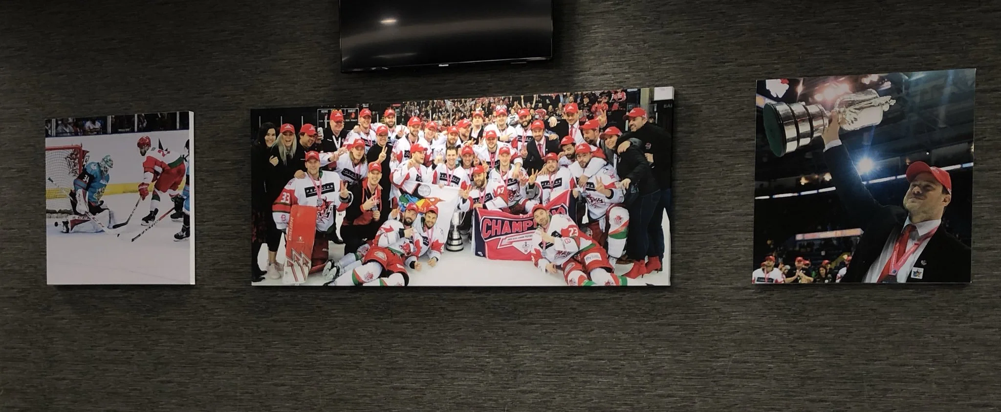 Group of hockey players and team members celebrating with a trophy, wearing red and white uniforms, with medals and a banner that says 'Champions'.