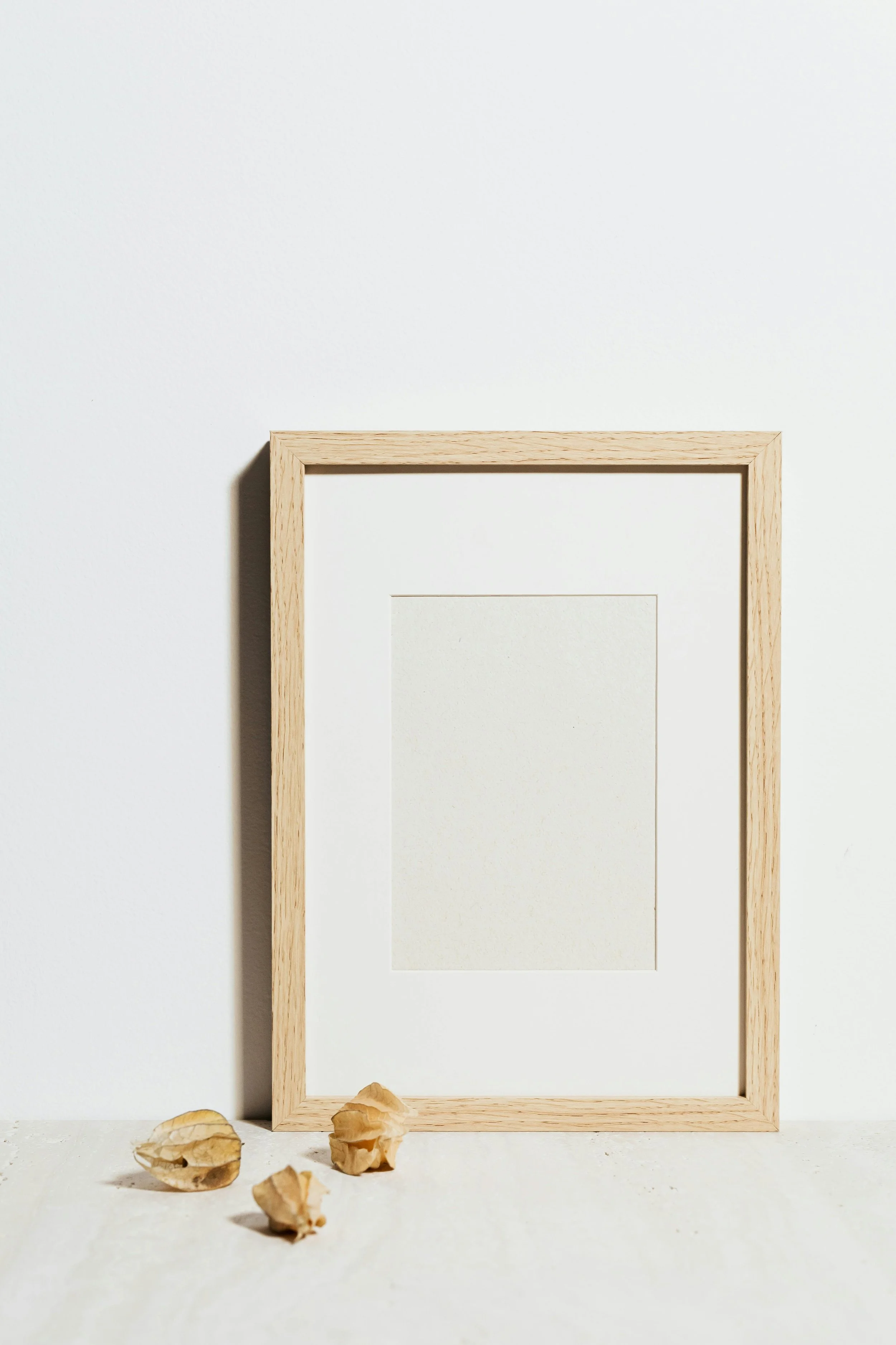 Empty picture frame with a wooden border on a white background, with three dried leaves at the bottom.