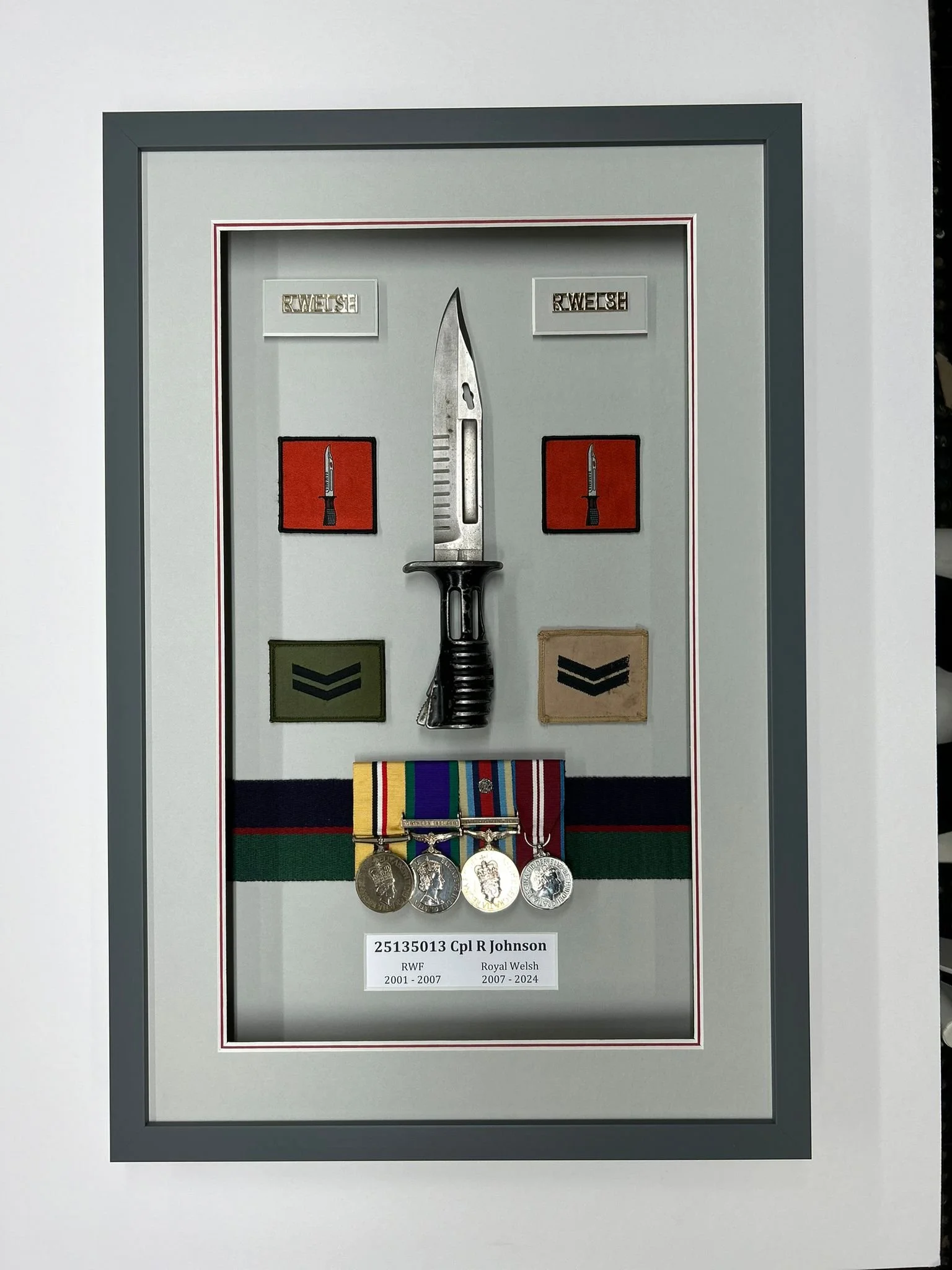 Display case with military medals, patches, a large knife, and labels indicating service periods of Cpl R Johnson in the Royal Welsh regiment from 2001 to 2024.