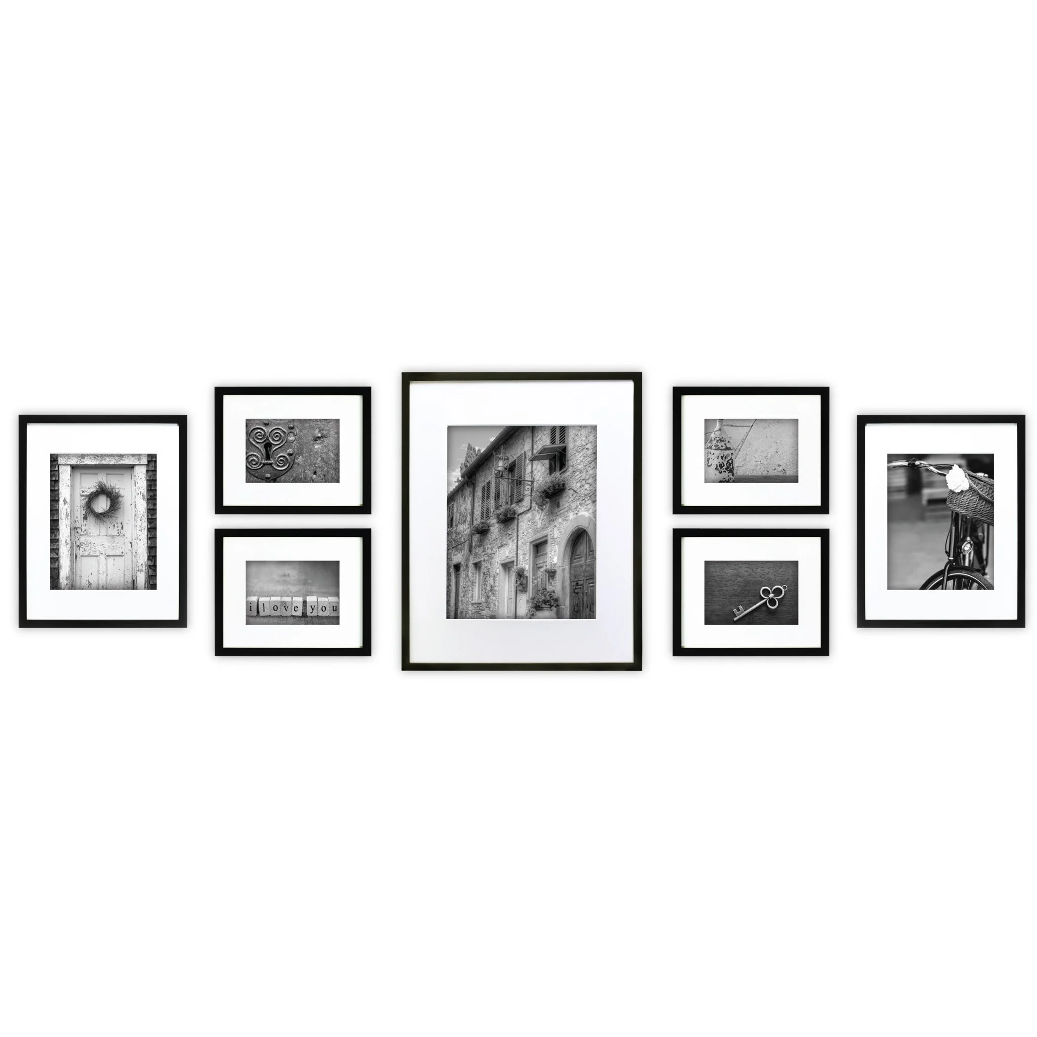 A wall display of seven black-and-white framed photographs of various objects and scenes, including a door, decorative spirals, a building facade, a bicycle, a key, a wall, and blocks spelling 'I love you'.