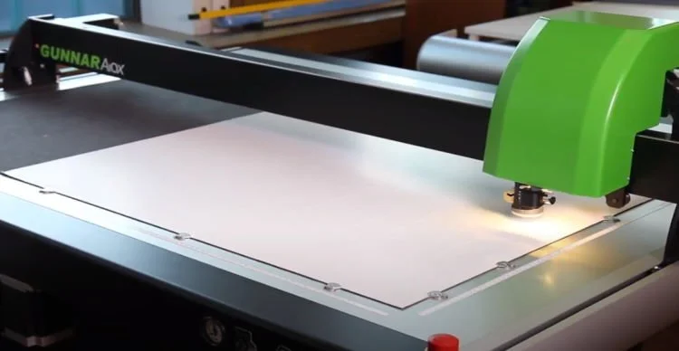CNC router machine with a cutting bit, engraving a white sheet of material in a workshop.
