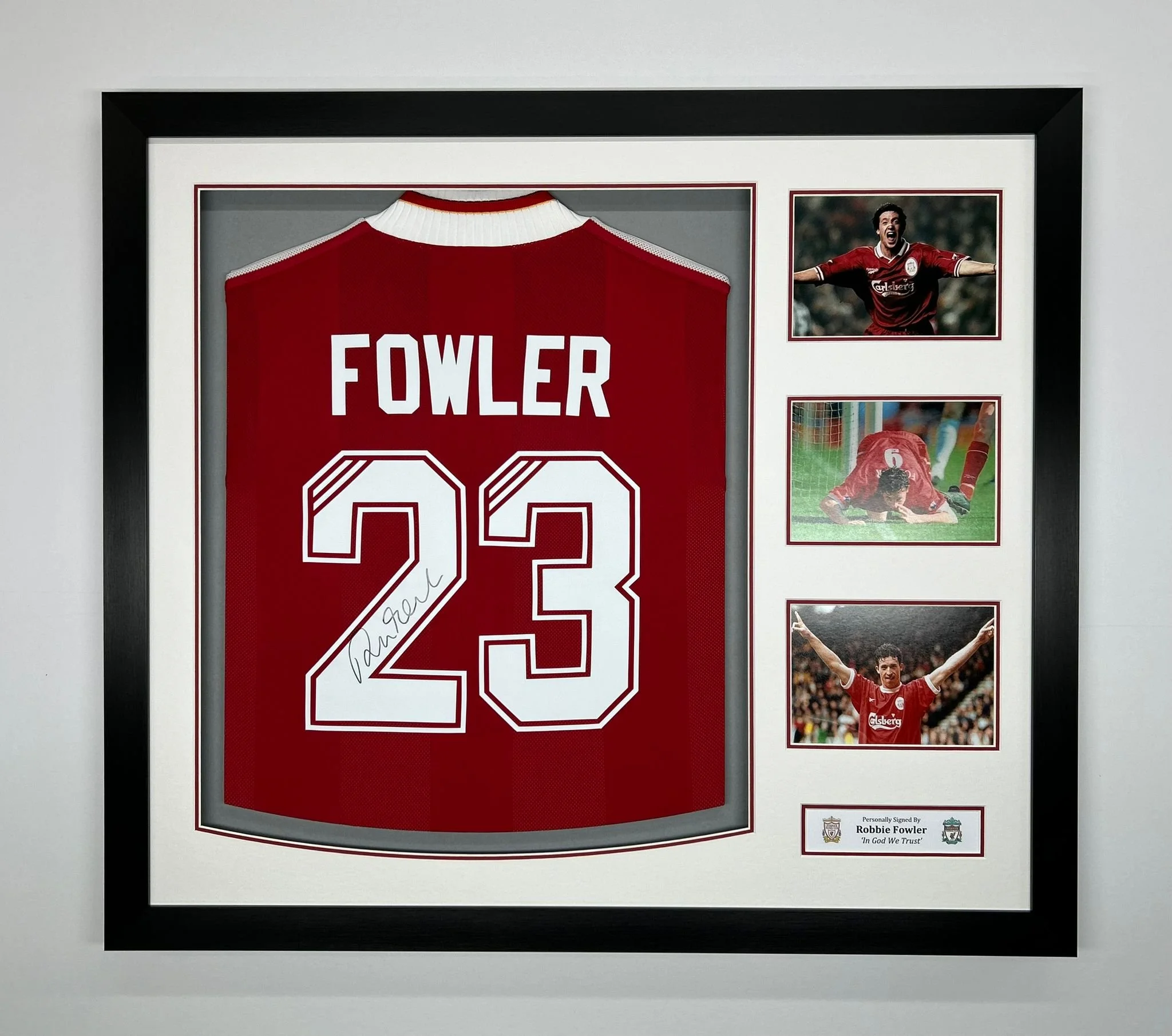 Framed display of a red soccer jersey with the name 'FOWLER' and number '23', signed on the number, along with three photographs of a soccer player celebrating, playing, and scoring, and a plaque stating 'Personally Signed By Robbie Fowler, In God We