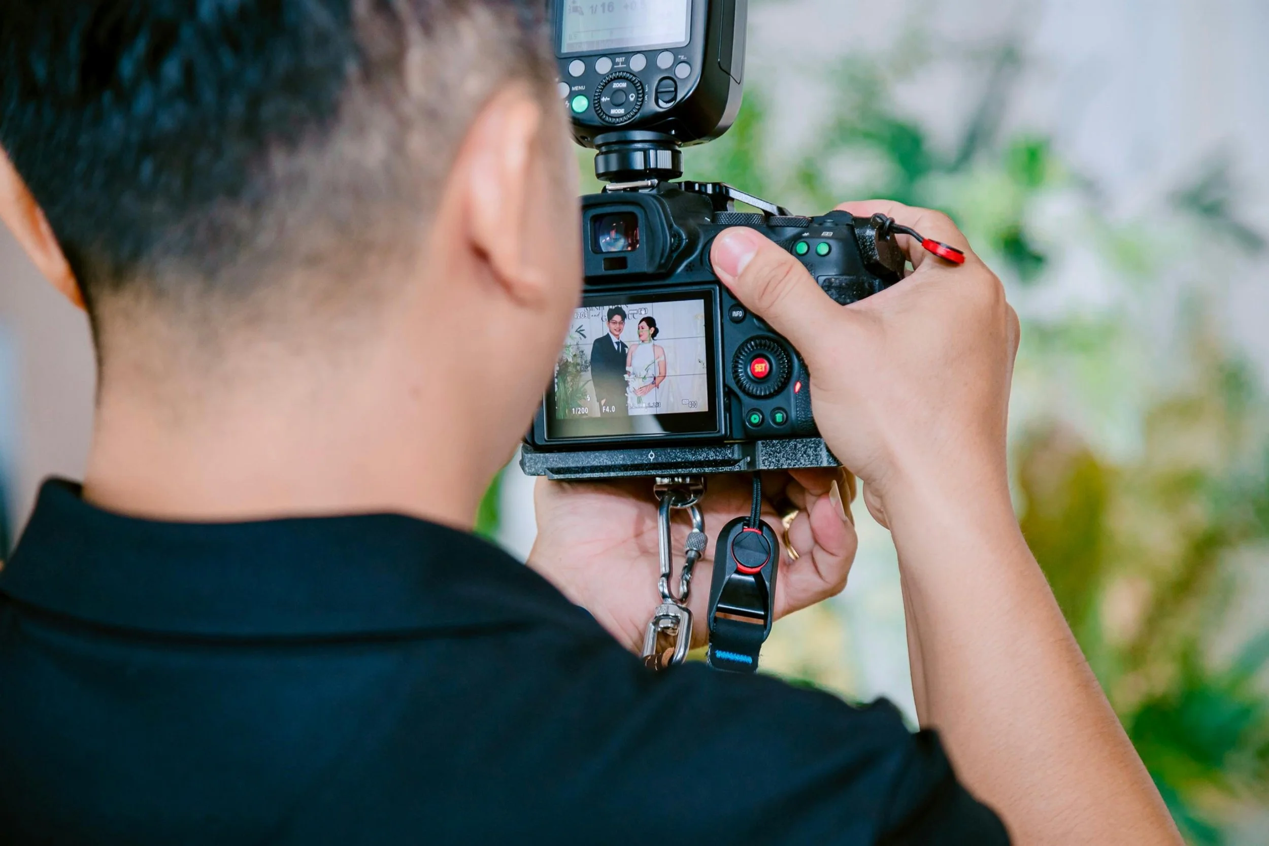 A photographer is taking a picture of two people with a professional camera, capturing their reflection on the camera's LCD screen.