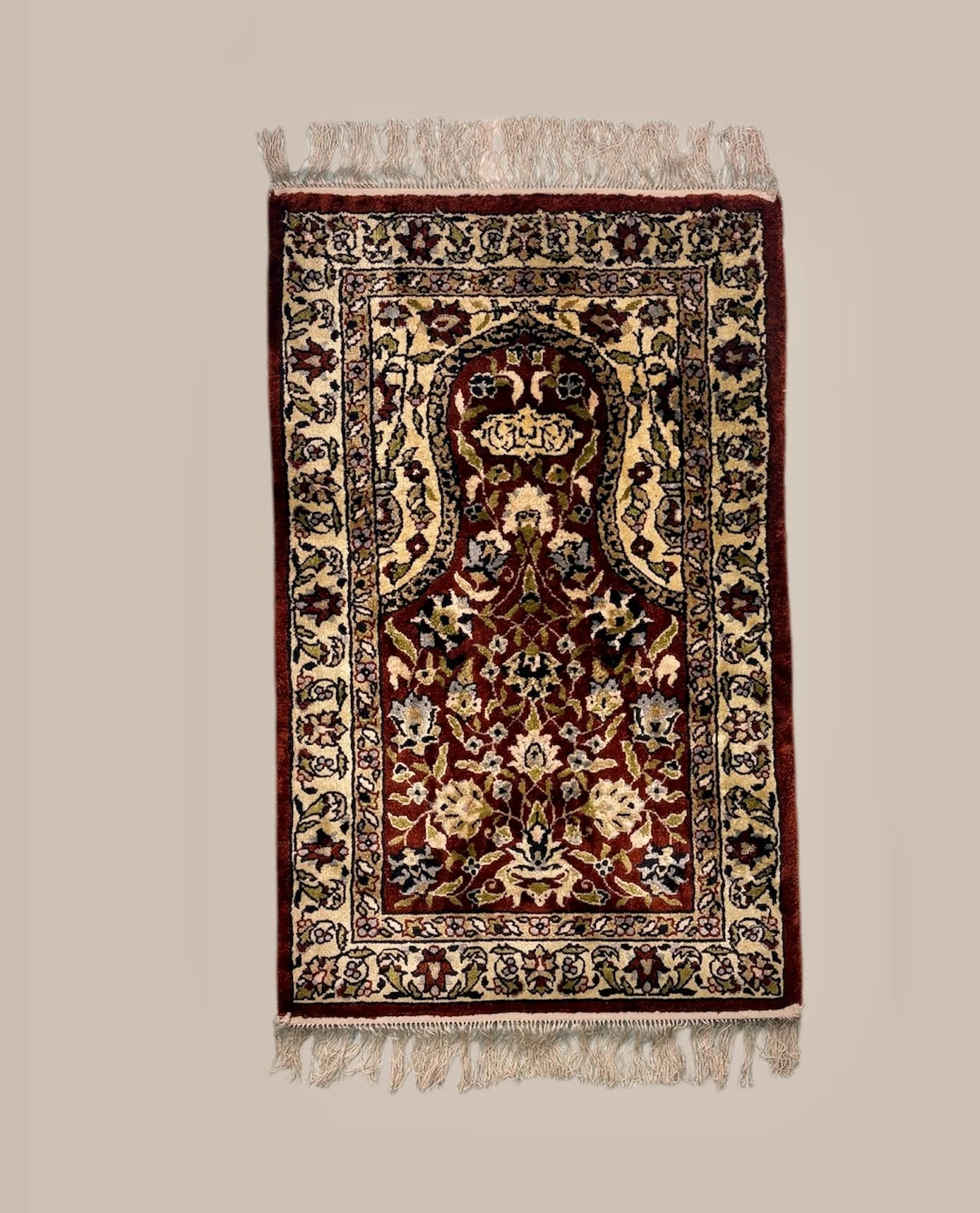 A decorated Persian-style rug featuring floral and geometric patterns, primarily in red, black, beige, and cream, with fringed edges.