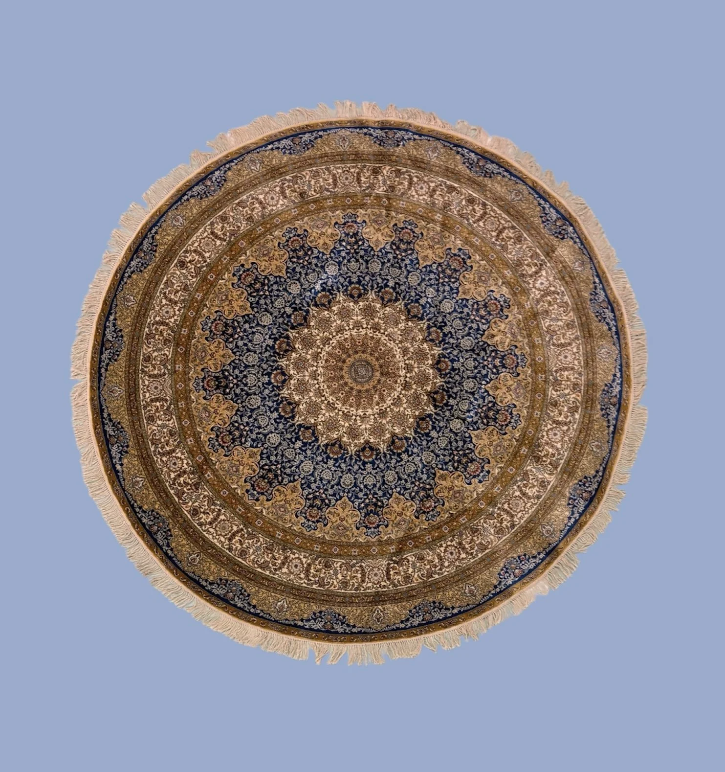A detailed Persian-style rug with intricate floral patterns in navy blue, gold, cream, and beige, fringed edges, placed on a plain blue background.