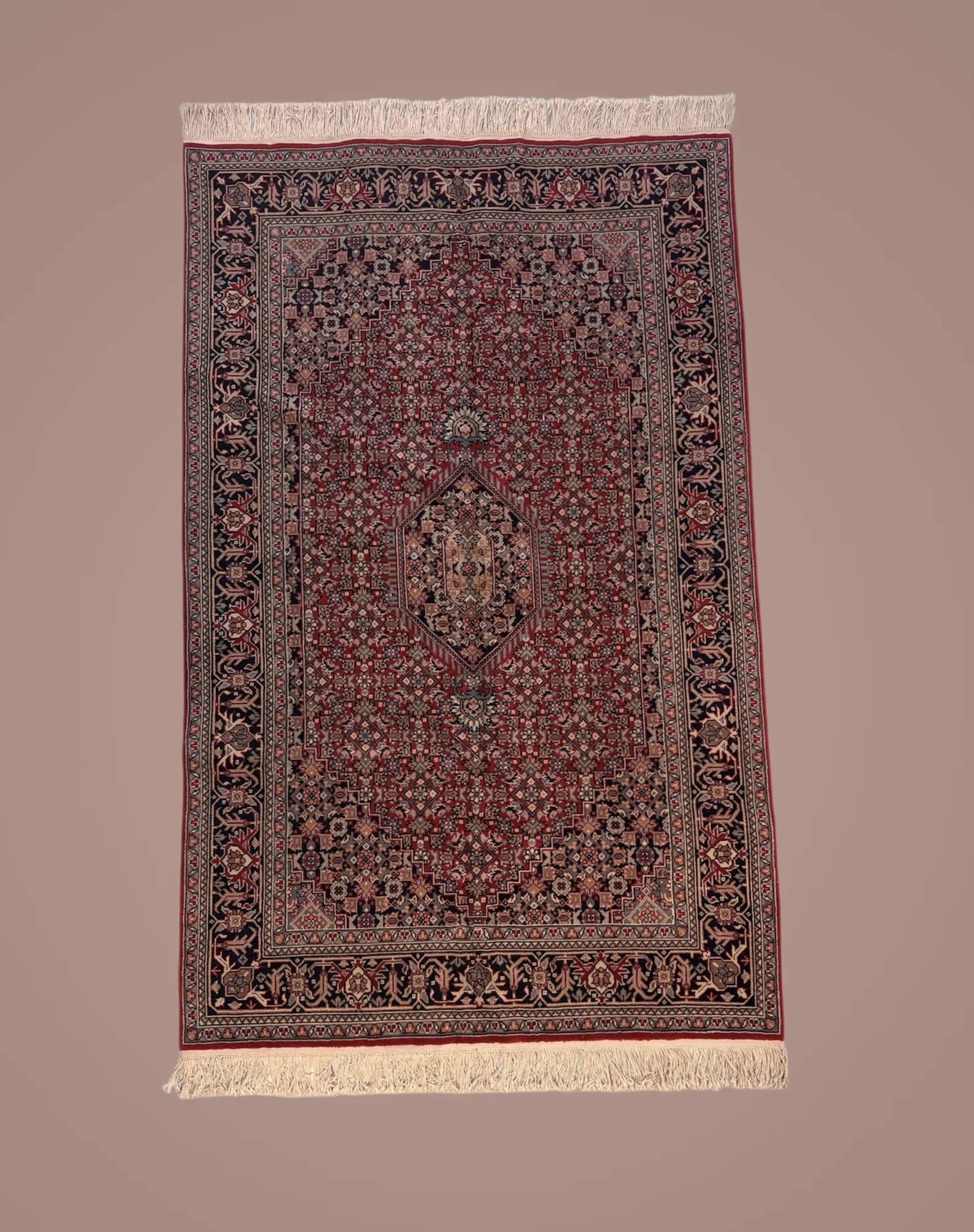 A detailed Persian-style rug with intricate floral and geometric patterns in red, black, and cream colors, and fringes on both ends.