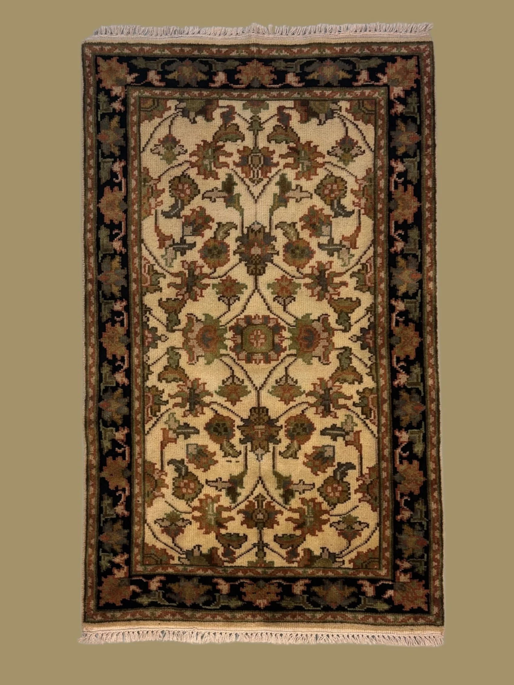 A decorative oriental rug featuring intricate floral and vine patterns in warm earthy tones, bordered by a black and red floral design, with fringed edges.