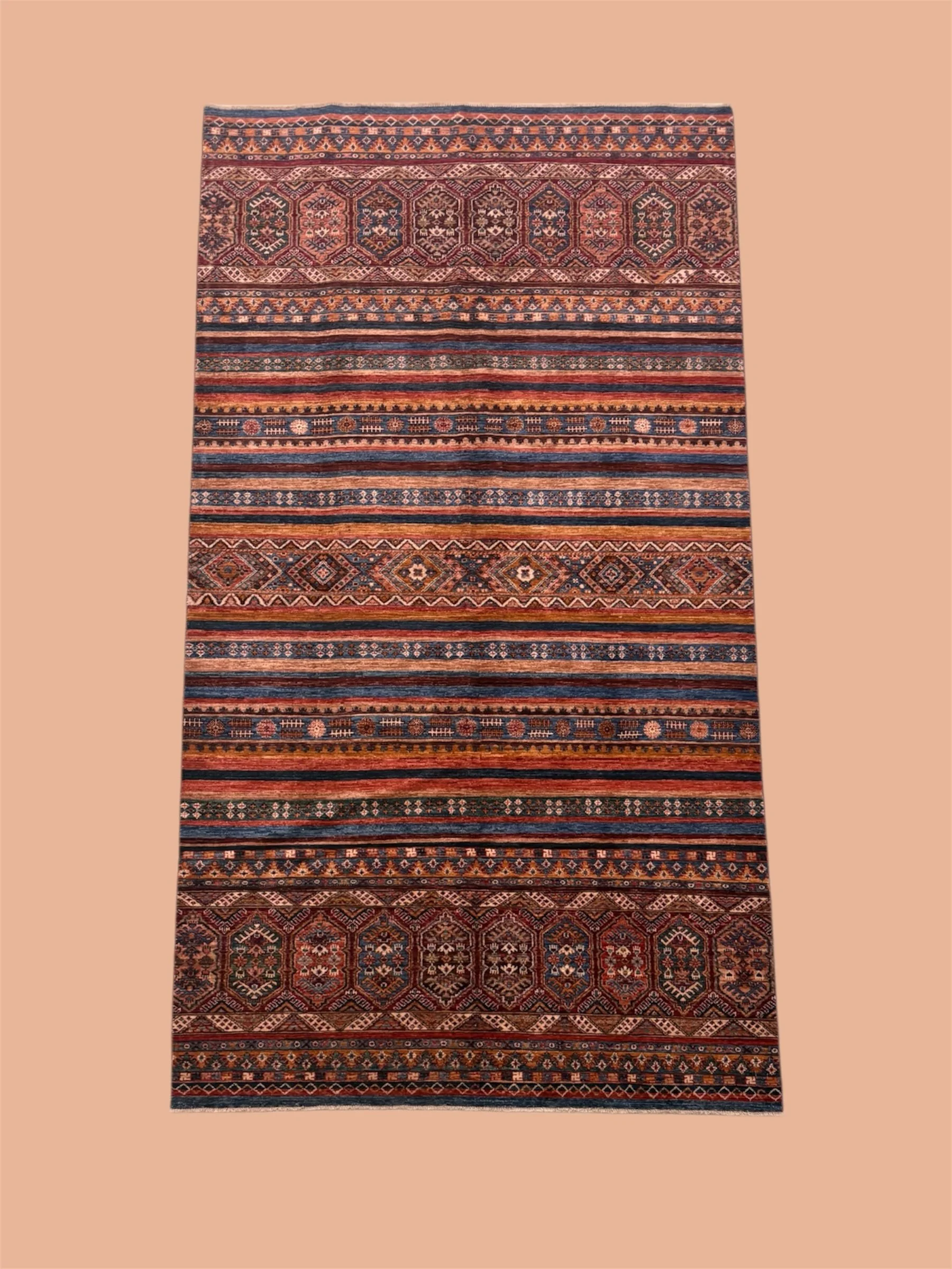 Colorful patterned area rug with intricate geometric and floral designs in shades of red, orange, blue, and beige, on a beige background.