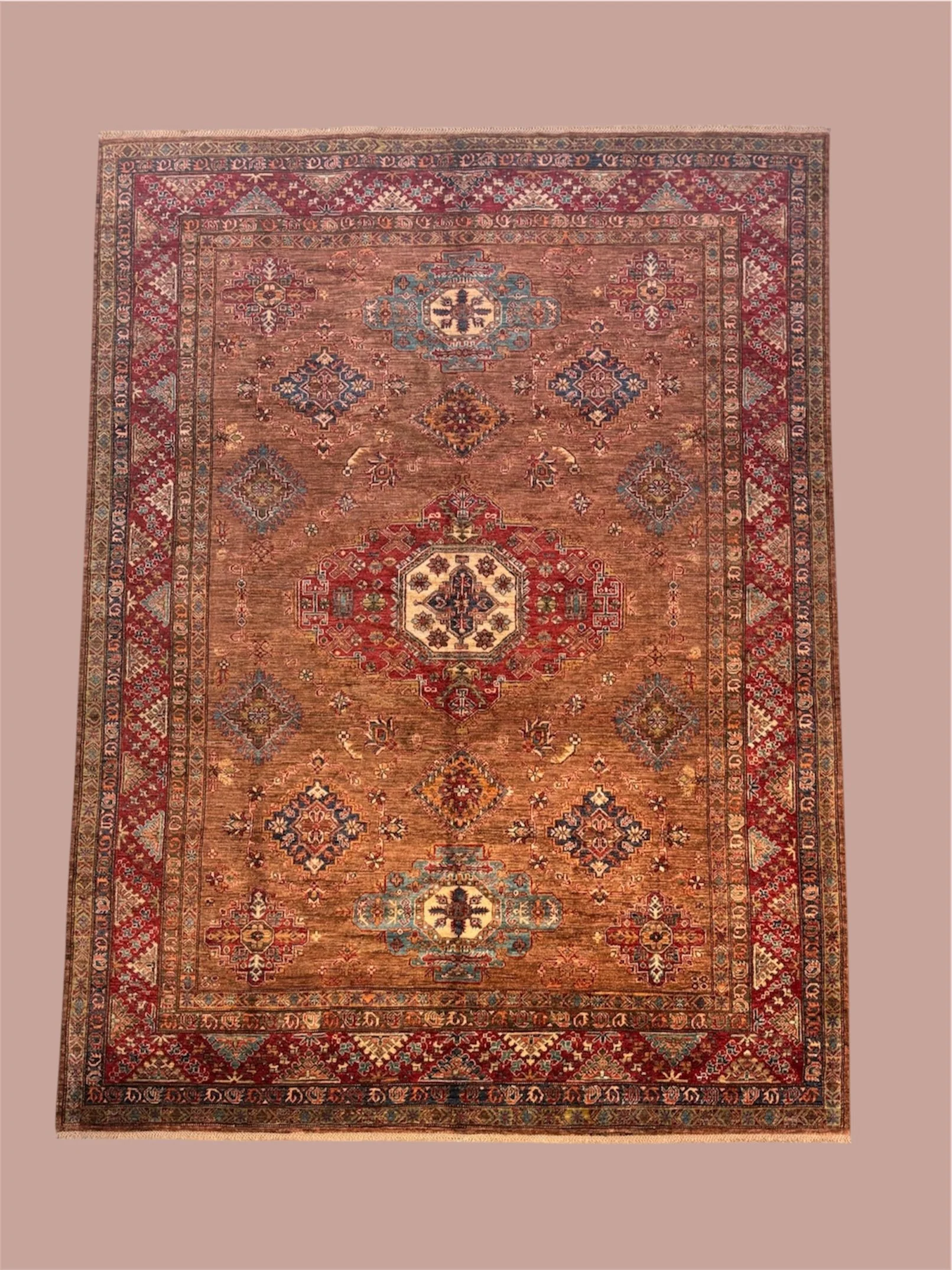 An ornate, traditional area rug with intricate patterns and multiple colors including red, blue, cream, and brown, placed on a pinkish-beige floor.