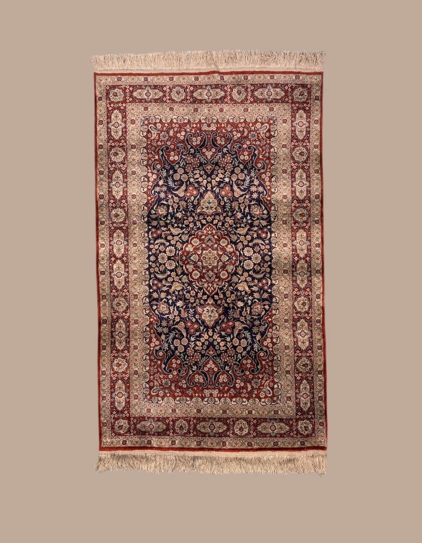 A traditional Persian-style area rug with intricate floral and geometric patterns in red, navy blue, beige, and cream, with fringed edges.