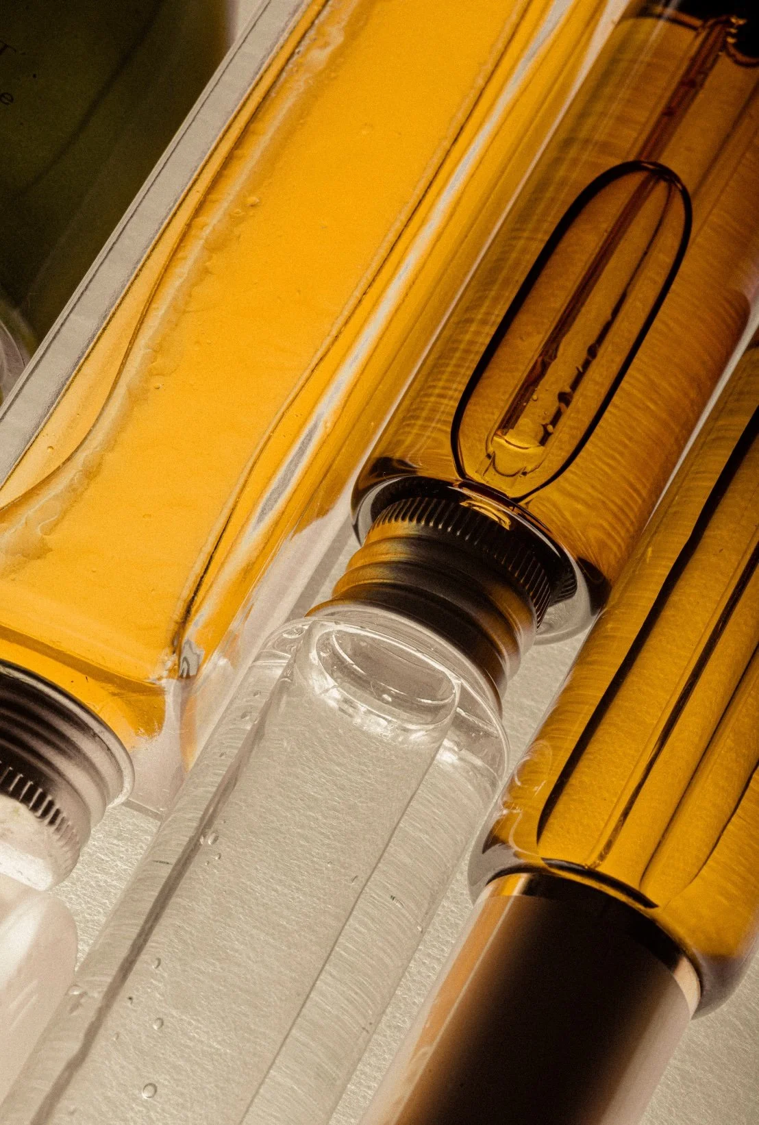 Close-up of two amber glass ampules and one empty glass ampule, with a yellow reagent on a metal surface.
