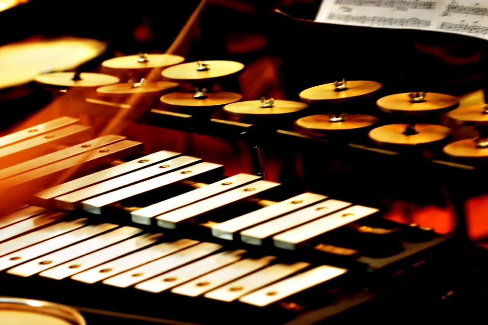 Close-up of a xylophone with metal and wooden bars and a set of cymbals in the background.