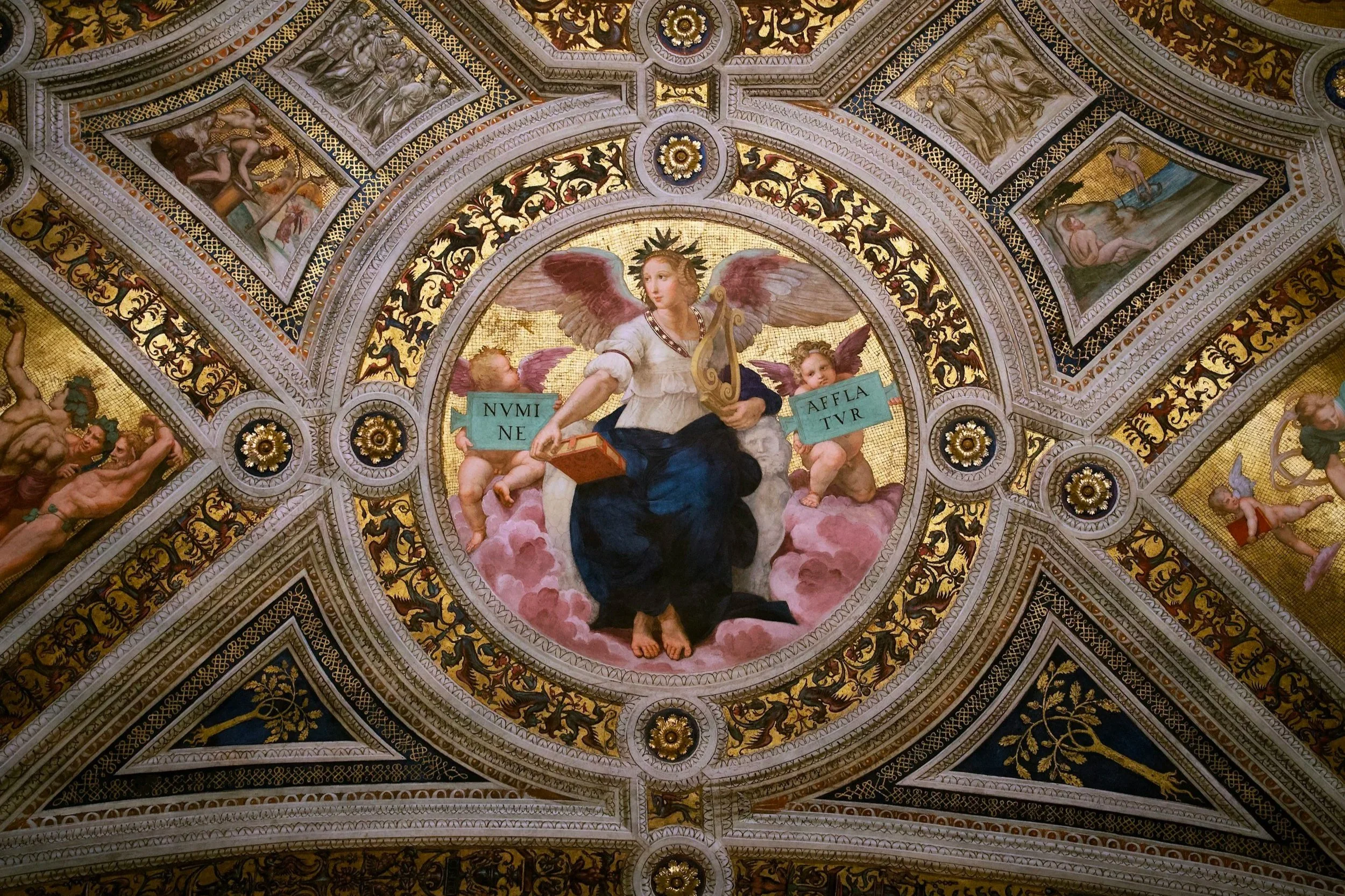 A detailed ceiling mural featuring a central depiction of an angel with pink wings holding a harp, sitting amidst clouds, surrounded by cherubs, angels, and ornate gold and white decorative patterns.
