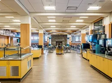 Empty cafeteria with yellow counters, beverage machines, and seating area.