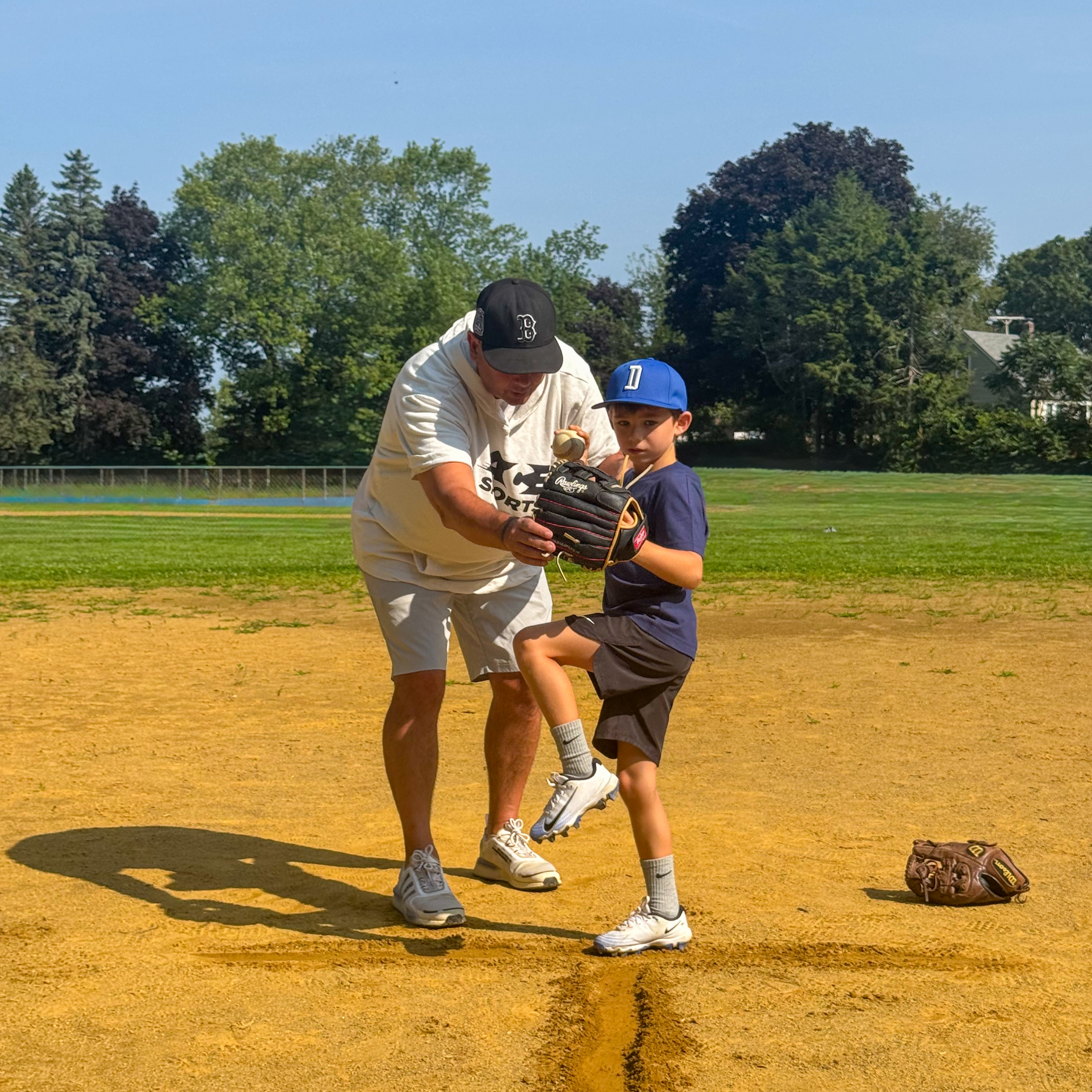An adult coach gives baseball instructions to a young boy on a dirt baseball field; the boy is in a baseball stance with a glove on his hand.