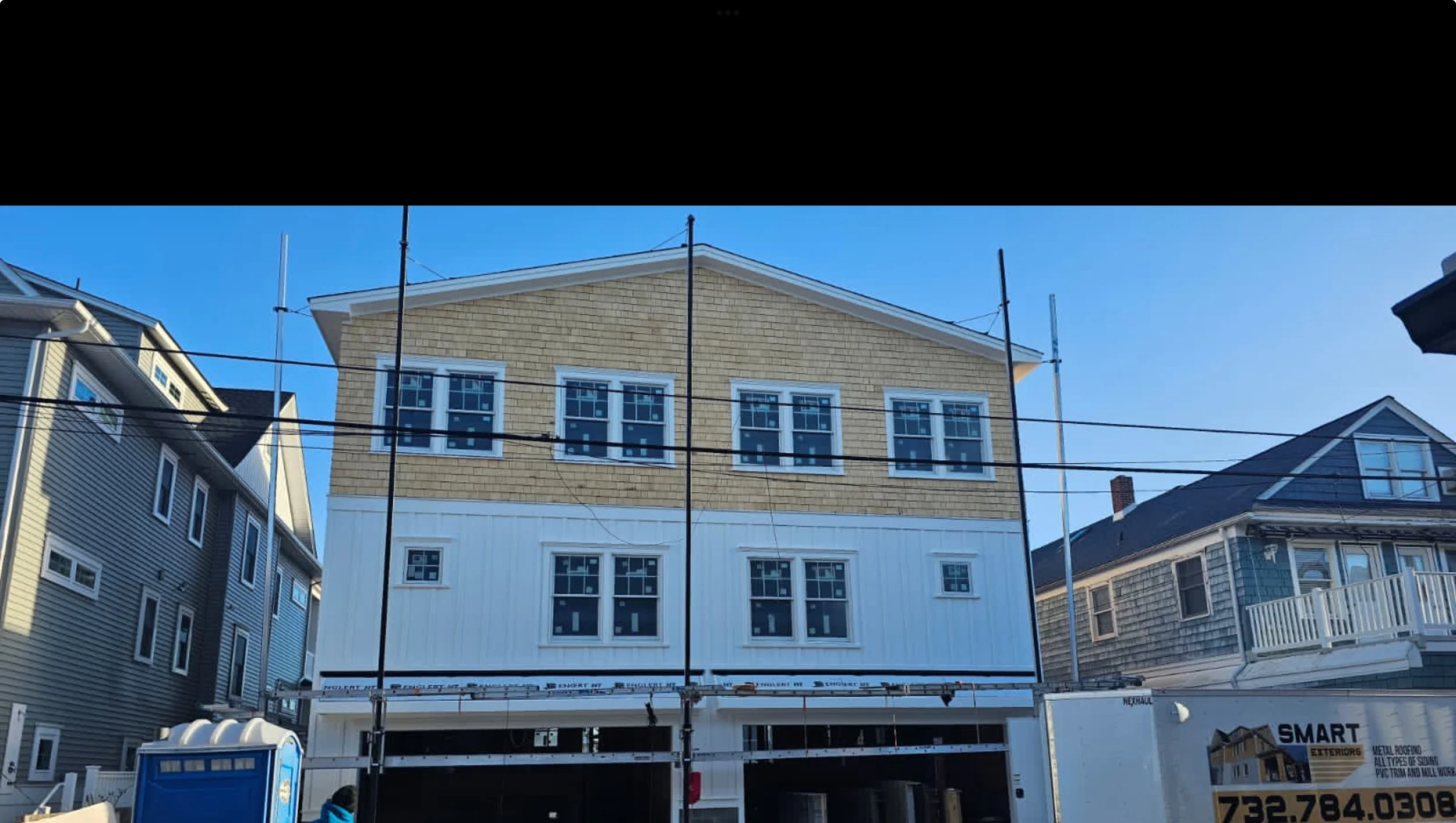 Under construction house with scaffolding and a neighboring house, blue sky