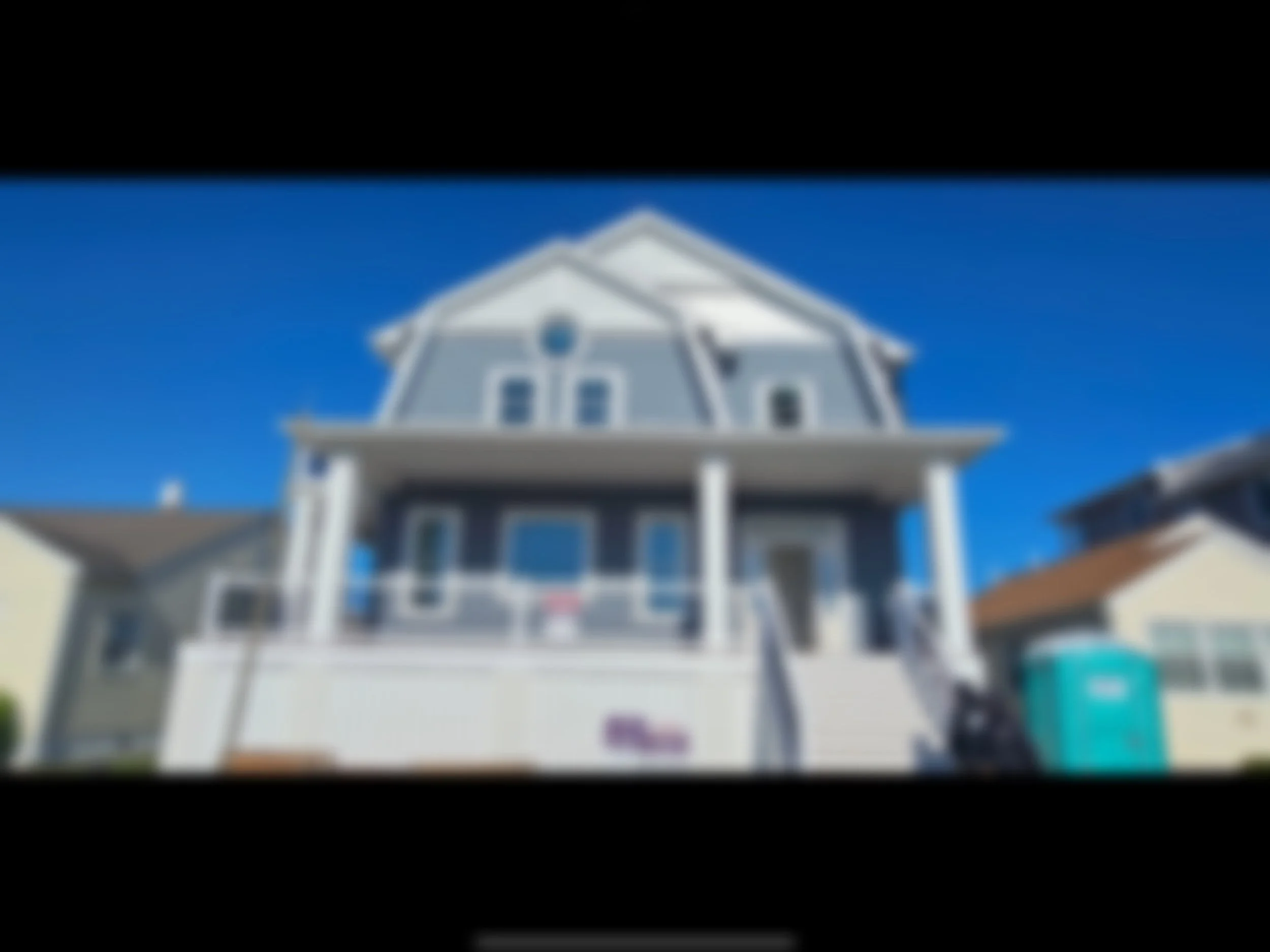 A blurred image of a two-story house with a porch, set under a blue sky.