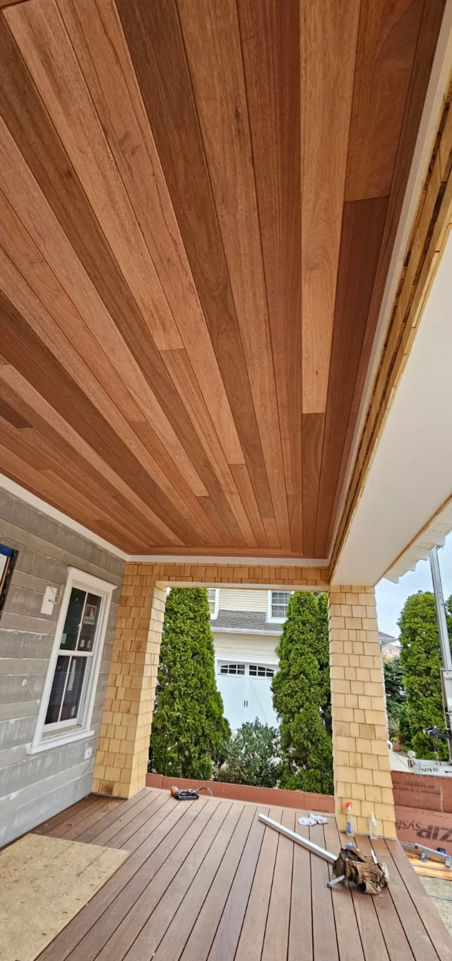 Under construction porch with newly installed wooden ceiling and flooring, tools, and building materials visible.