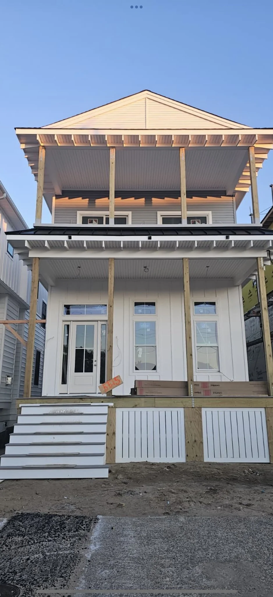 Front of a house under construction with stairs and porch, with some wooden supports and new siding, during daytime.