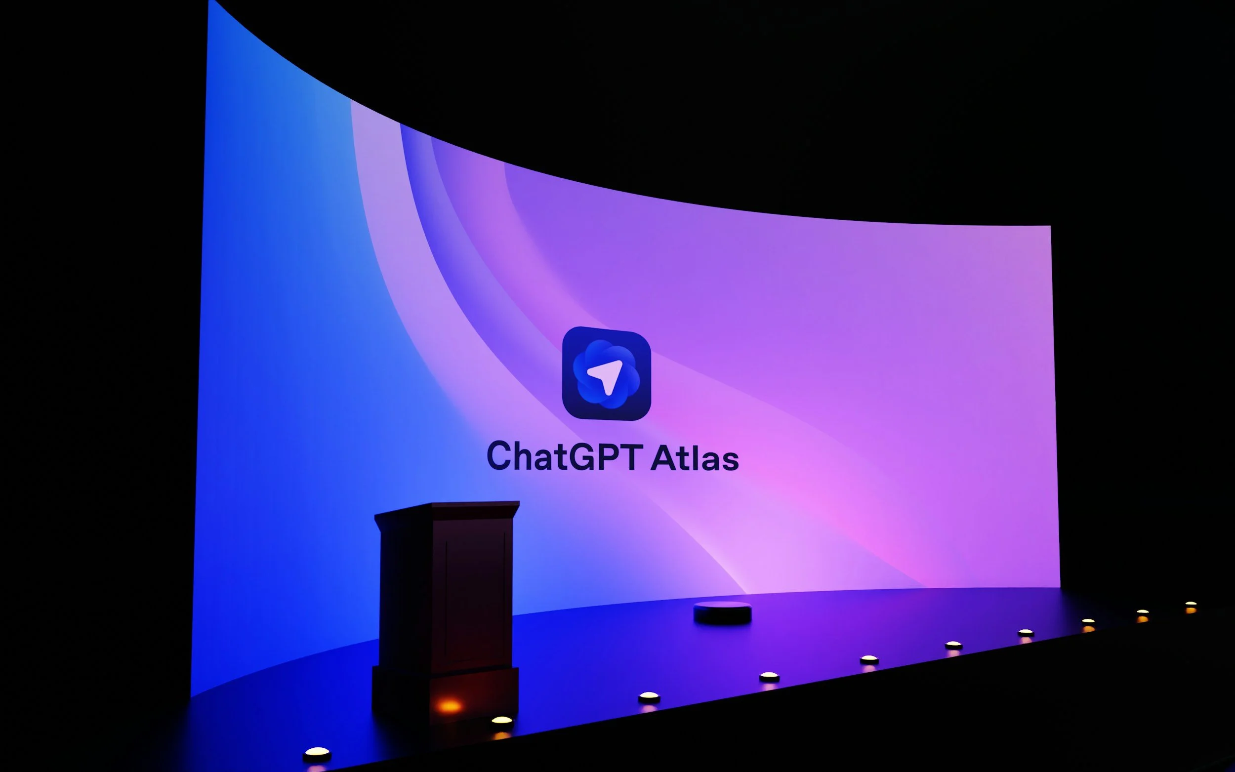 Large screen displays the ChatGPT Atlas logo with purple and blue gradient background, a podium stands in front of the screen, and small lights line the stage floor.