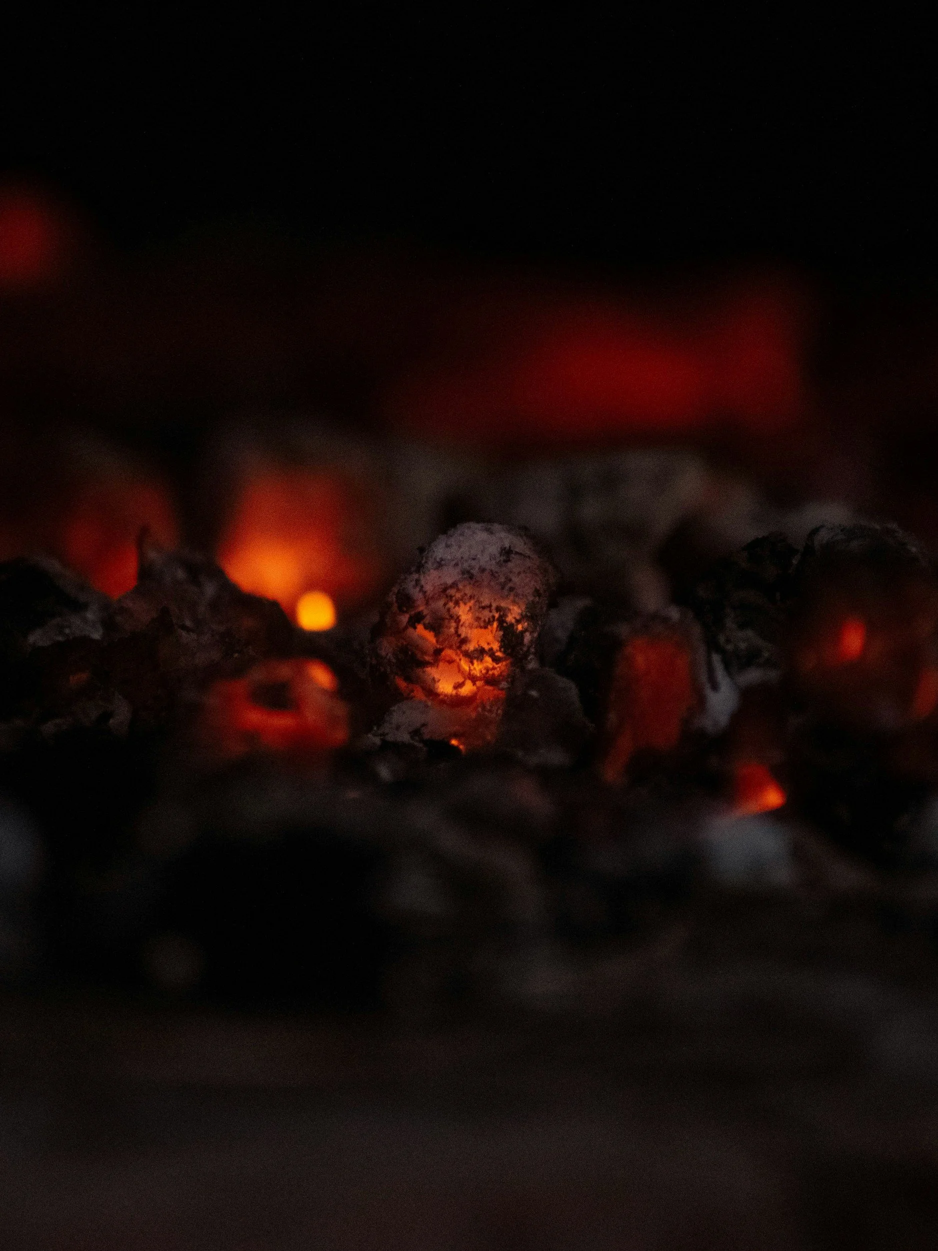 Close-up of glowing red and orange embers and ashes on charcoal or burning wood in a dark setting.