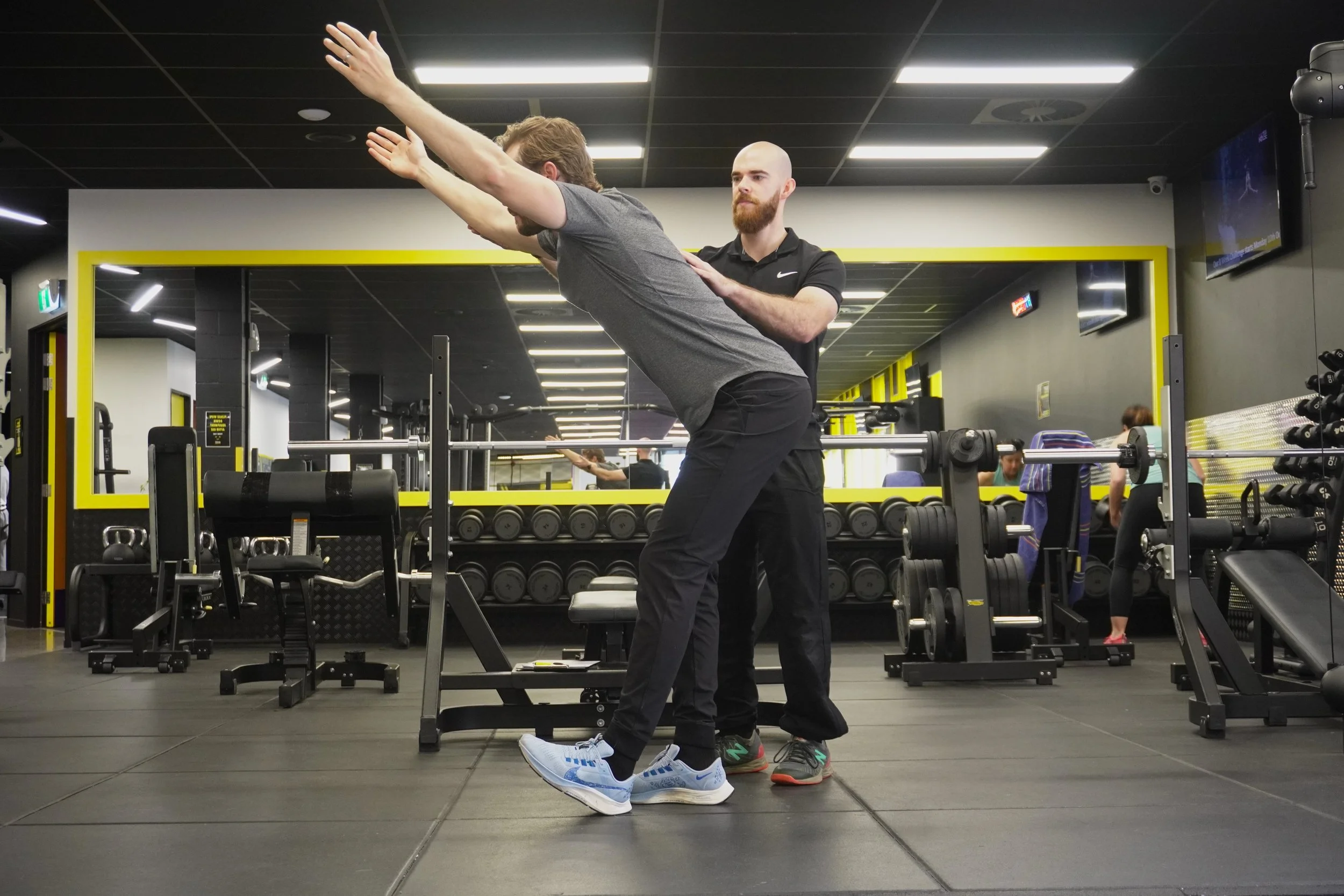 A man performing a stretch in a gym room being guided by Precision Fitness personal trainer