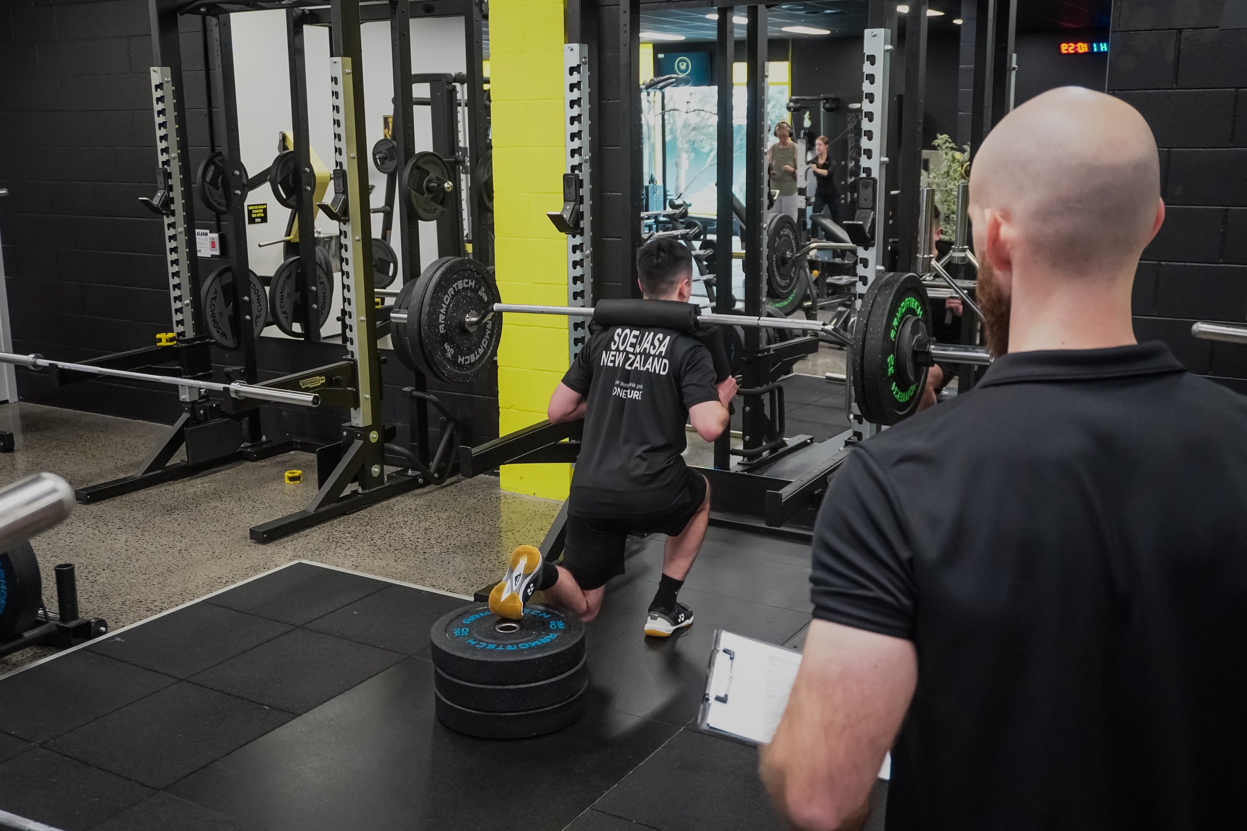 Man in gym lifting weights while being guided by Precision Fitness personal trainer