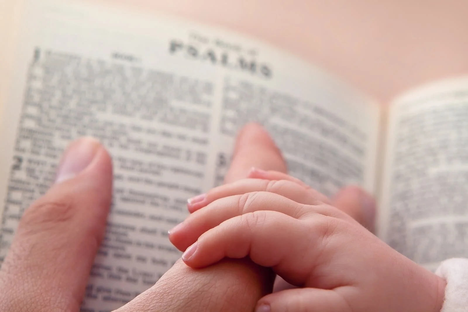 Baby's hand resting on an adult's hand over an open Bible turned to the book of Psalms. Learn how I-cbt in provo, ut can help during religious scrupulosity treatment.