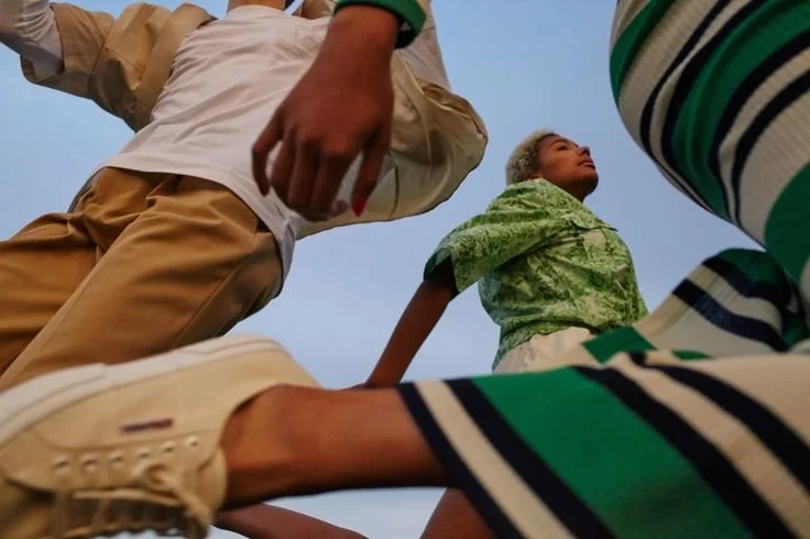 Low-angle view of young people gathered outdoors, some sitting, some standing, against a clear sky, seen from beneath.