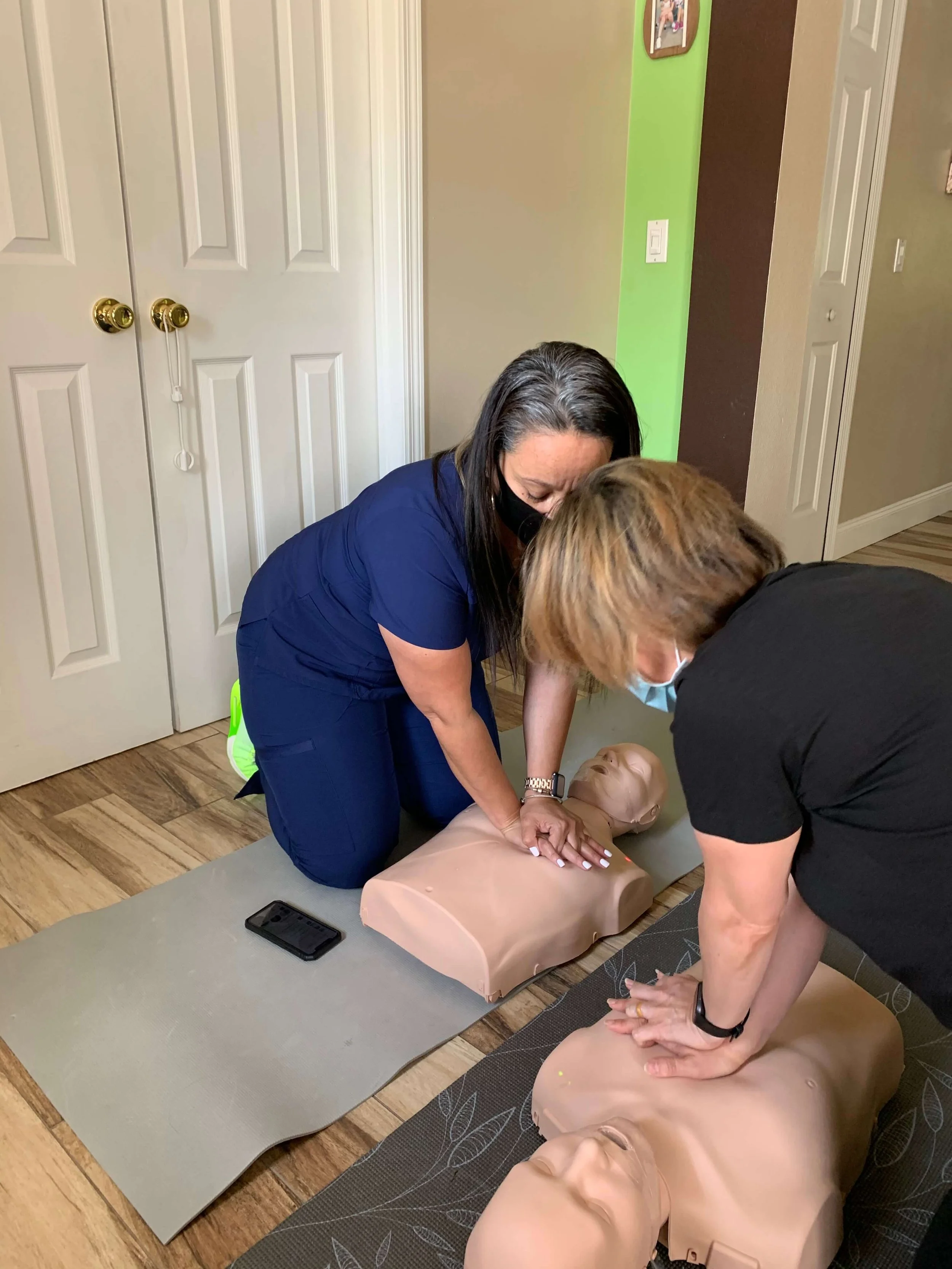Two women practicing CPR on adult mannequins in a training session.