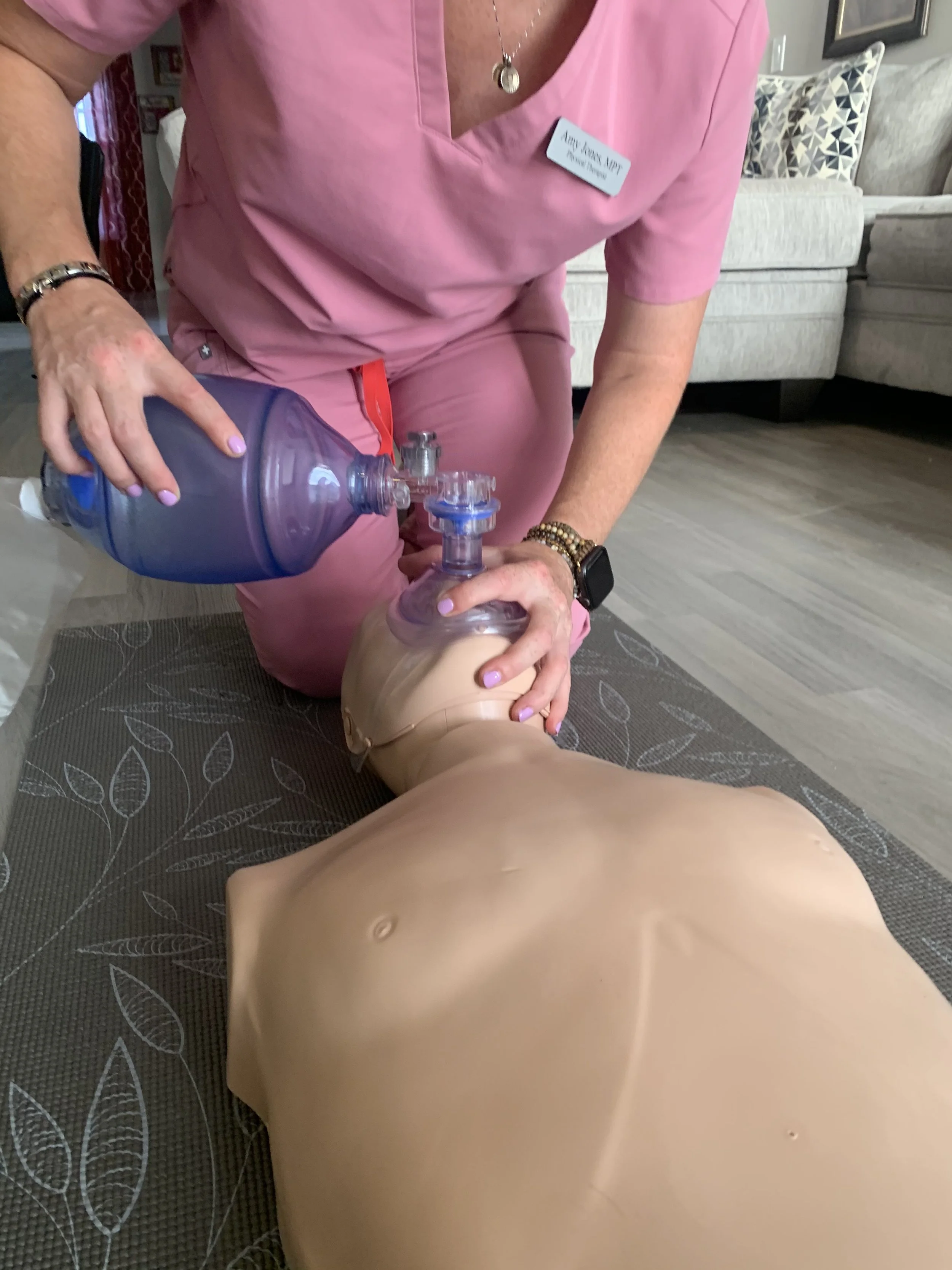 A person in pink scrubs performing CPR with a bag-valve mask on a medical training mannequin.