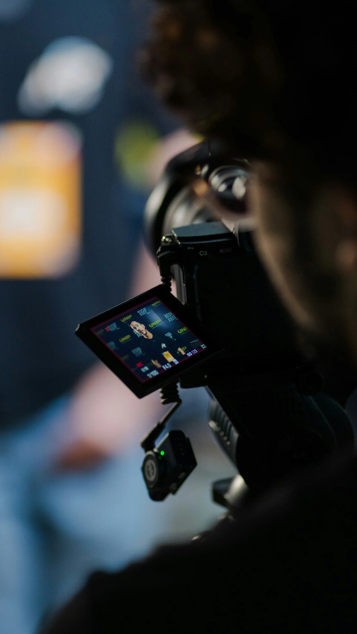 A person is capturing a photo or video with a camera mounted on a tripod. The camera's display screen shows a woman posing for the shot.