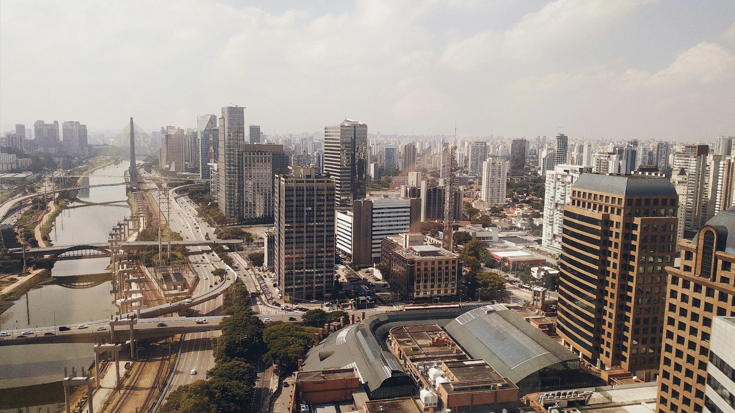City skyline with tall buildings, a river, bridges, and roads viewed from a high vantage point during daytime.