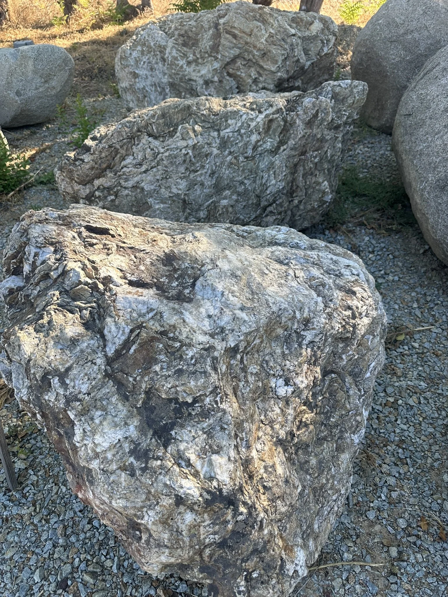 Multiple large rocks and stones in an outdoor setting with some small plants and dirt around them.
