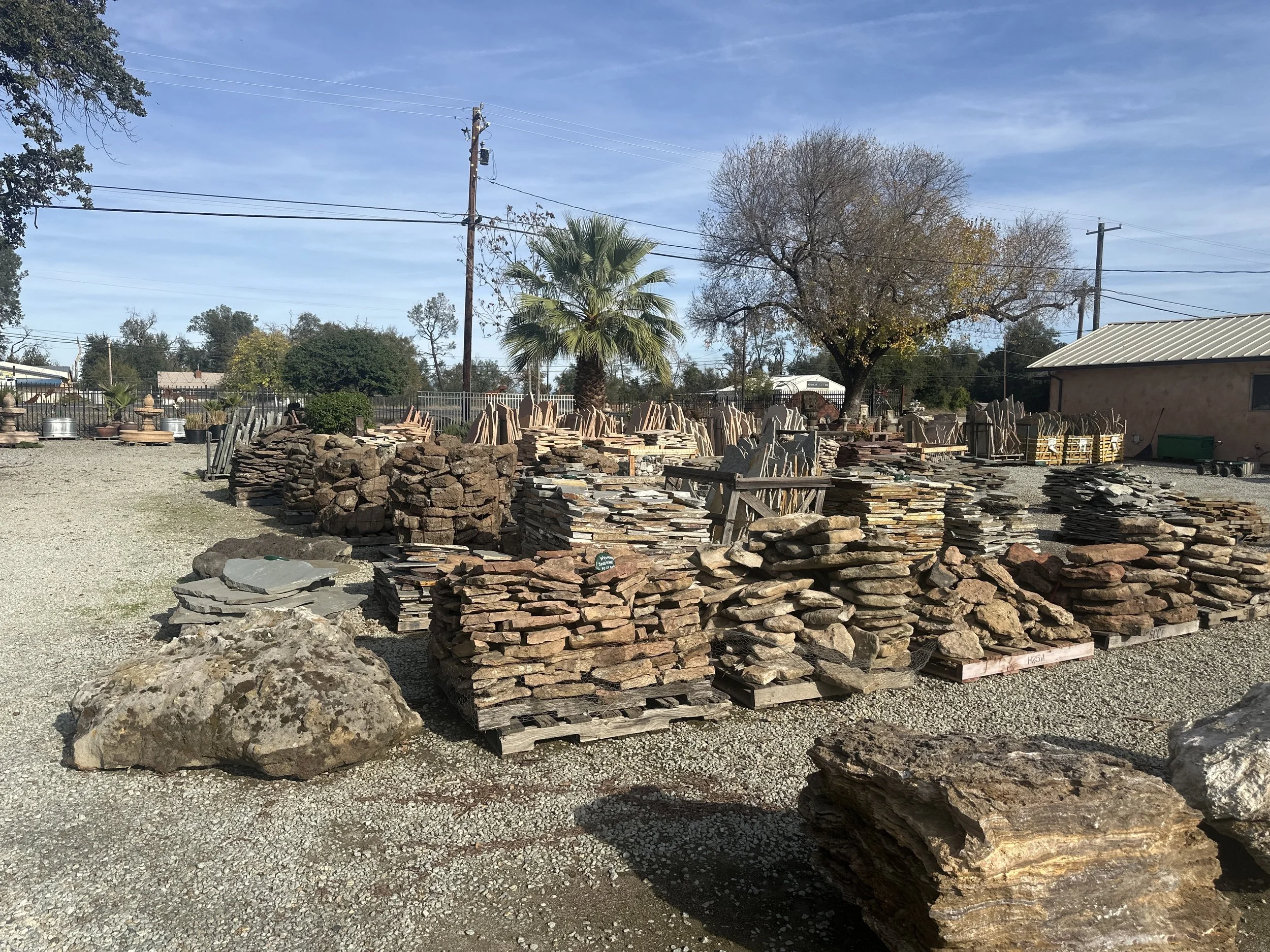 Outdoor display of stacked stones and rocks with trees and utility poles in the background.