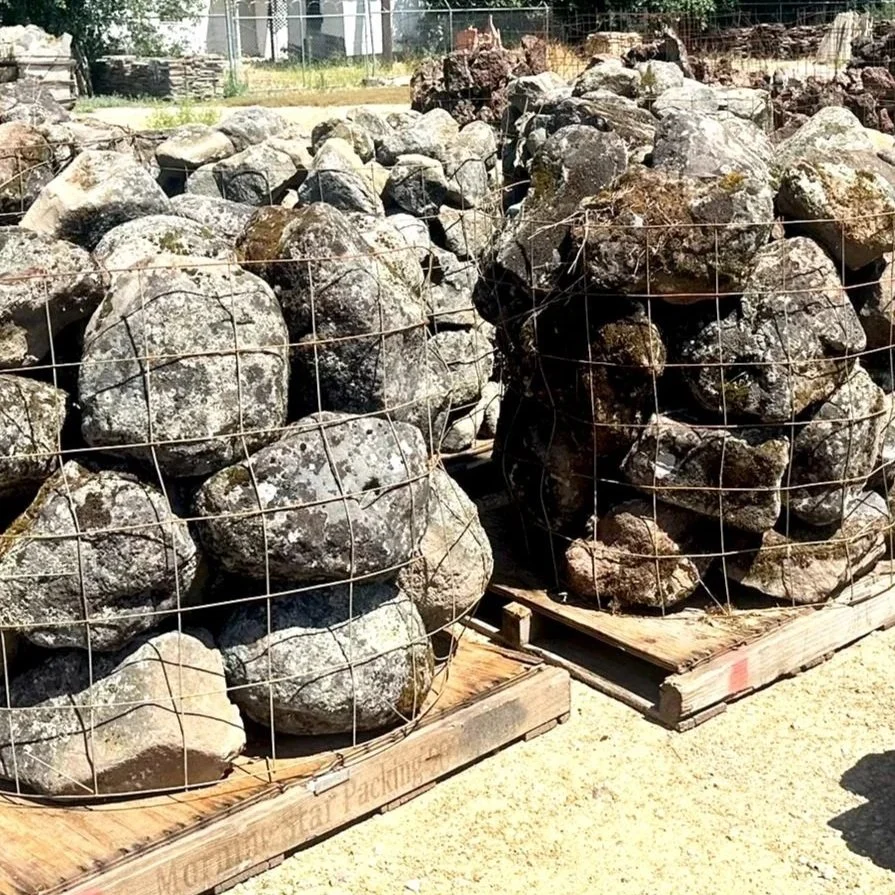 Two stacks of field moss small boulder rocks enclosed in wire mesh, placed on wooden pallets outside.