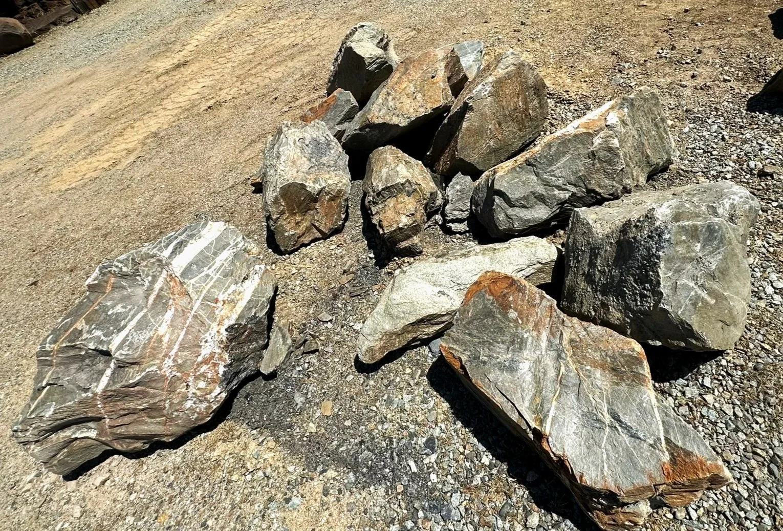 White and Black Slate large rocks and boulders scattered on a dirt surface outdoors.