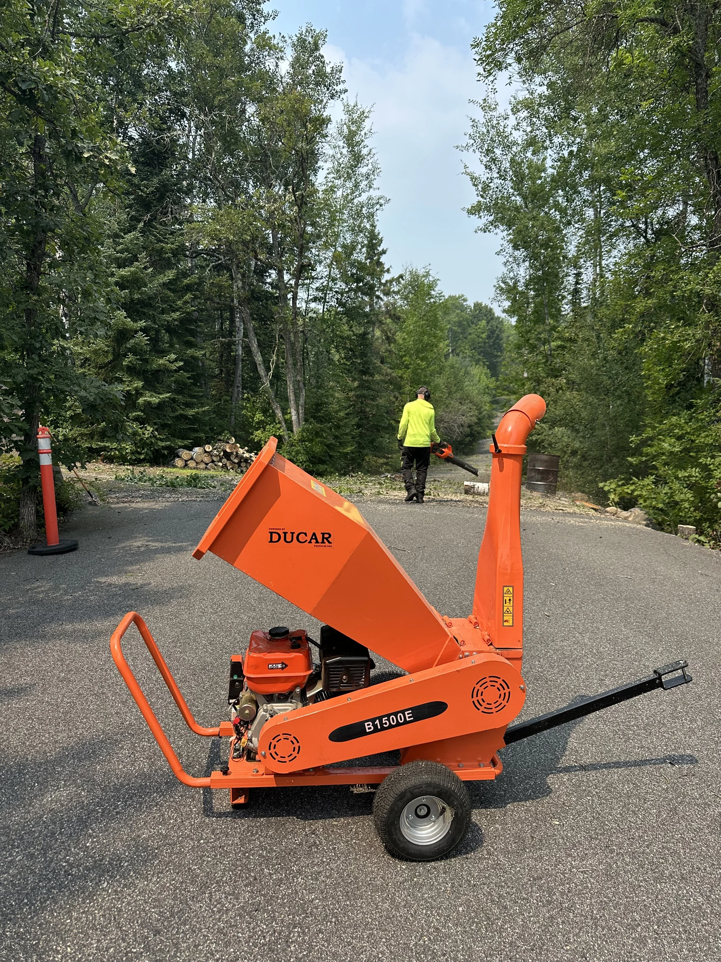Two people wearing helmets with a trailer loaded with twigs and branches in a wooded area.