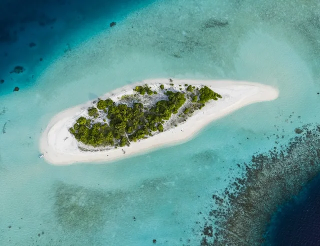 A small, sandy island with dense green trees surrounded by clear turquoise water.