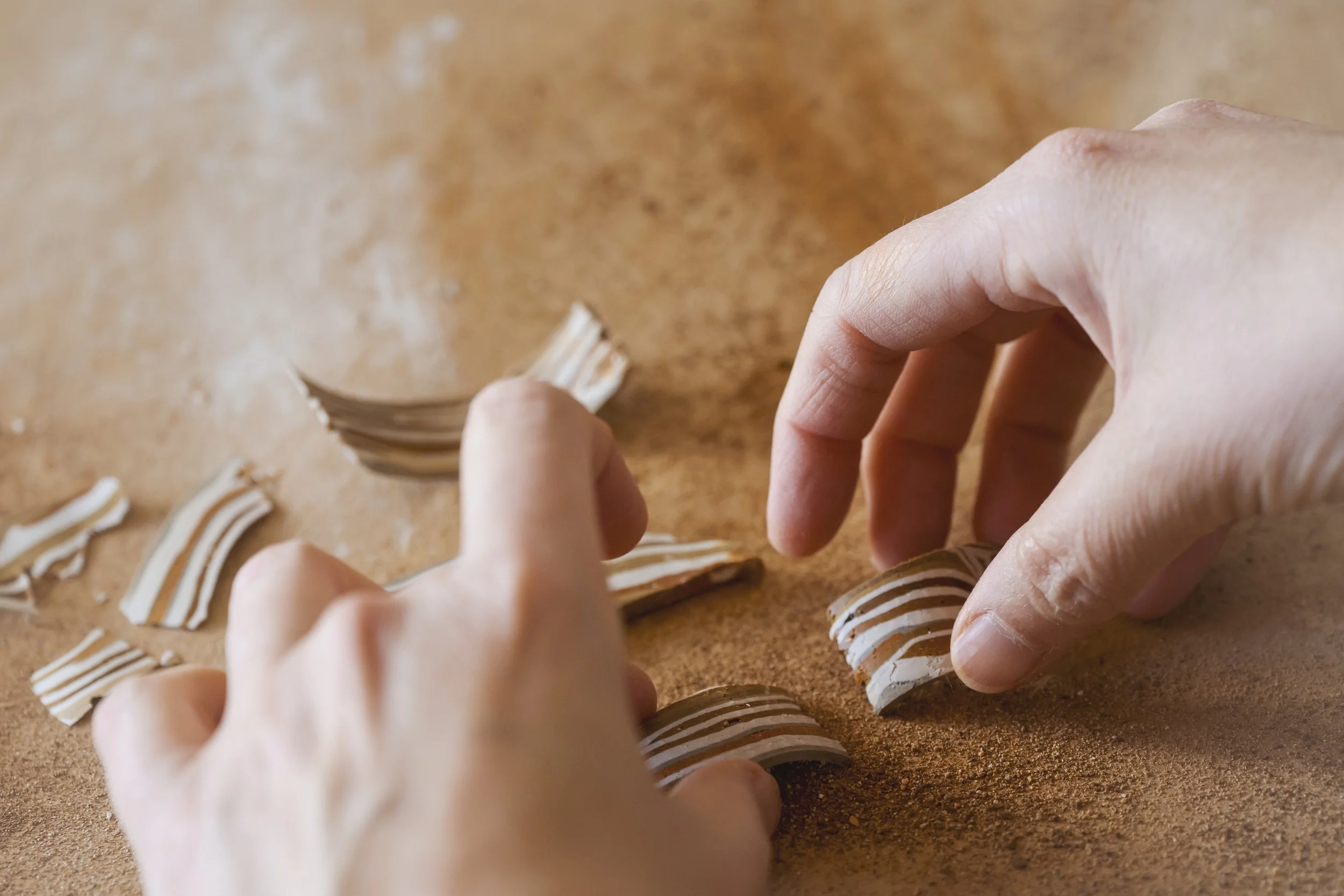 Hands arranging or creating striped pieces of a material on a brown surface.