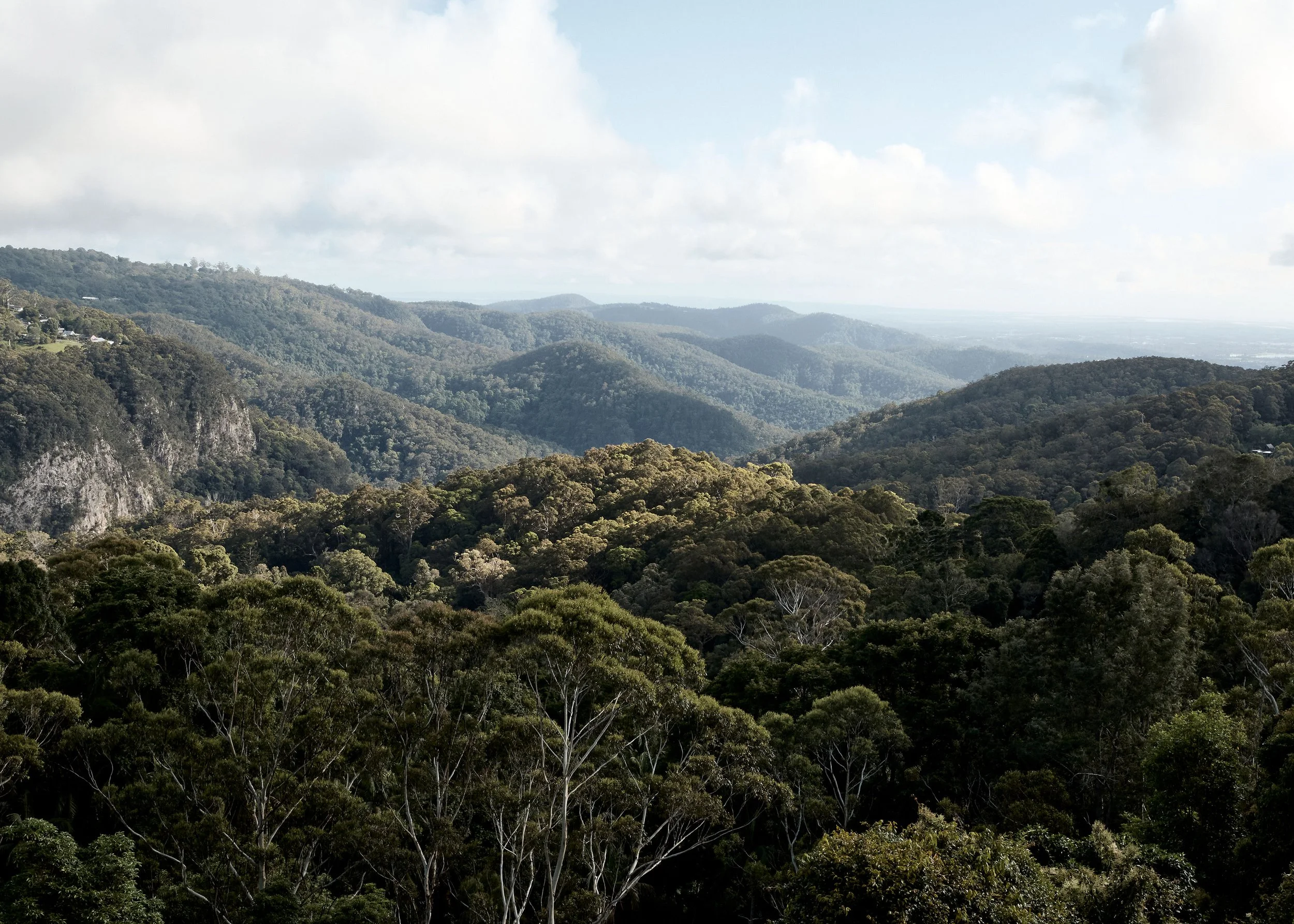 A view of lush green mountains and forested hills under a partly cloudy sky.