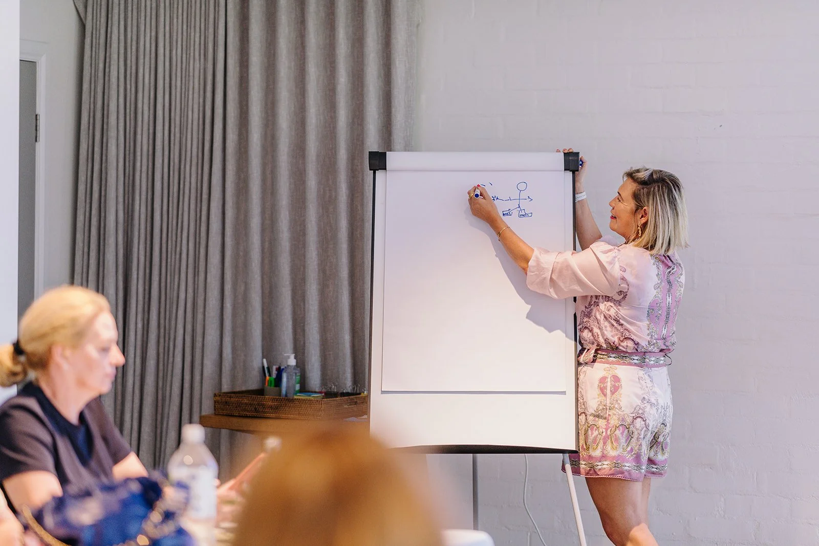 Woman giving presentation in front of a flip chart with a diagram, seated audience with a woman in the foreground