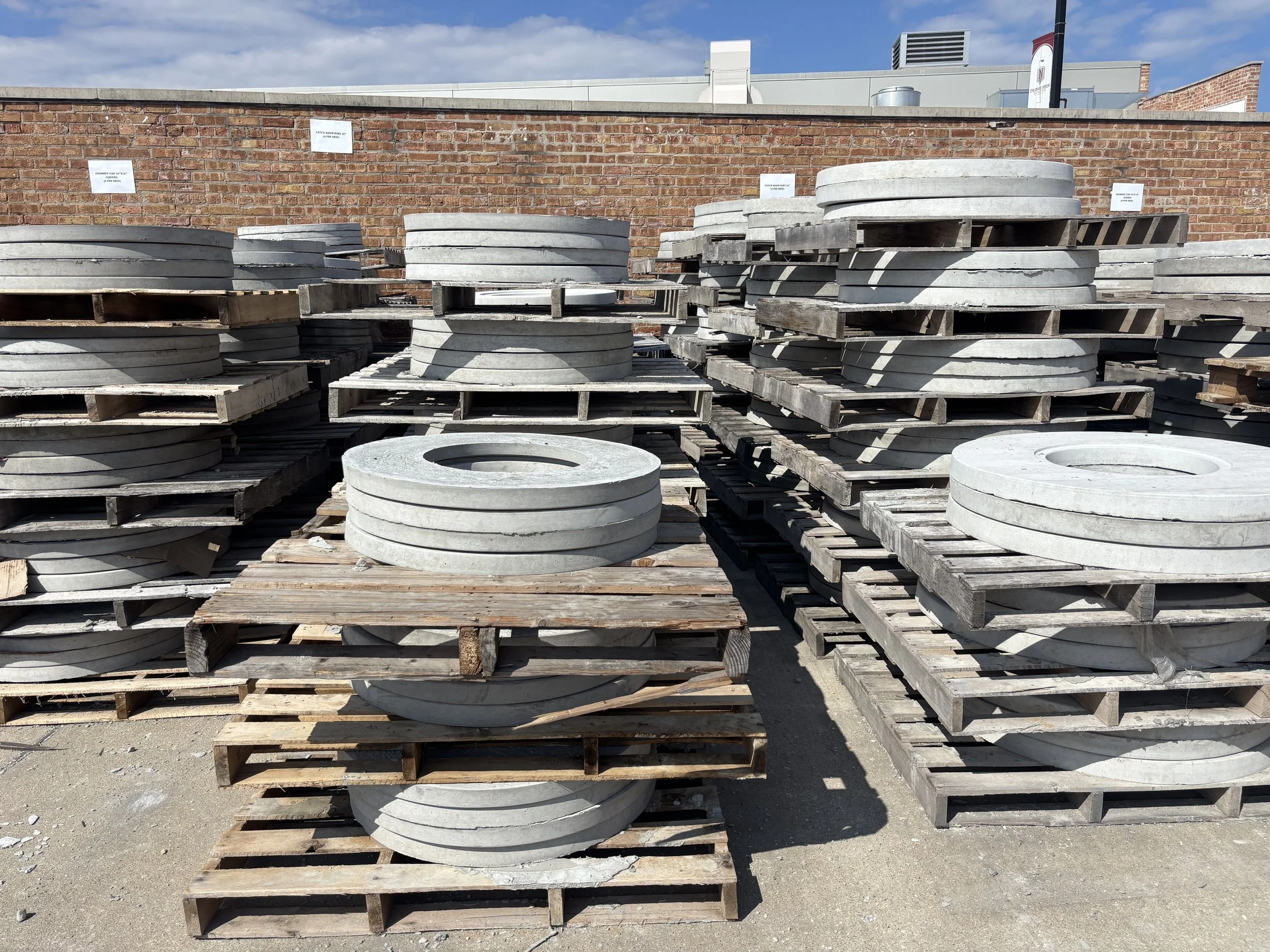 Stacks of large, round concrete manhole covers on wooden pallets at a construction supply yard
