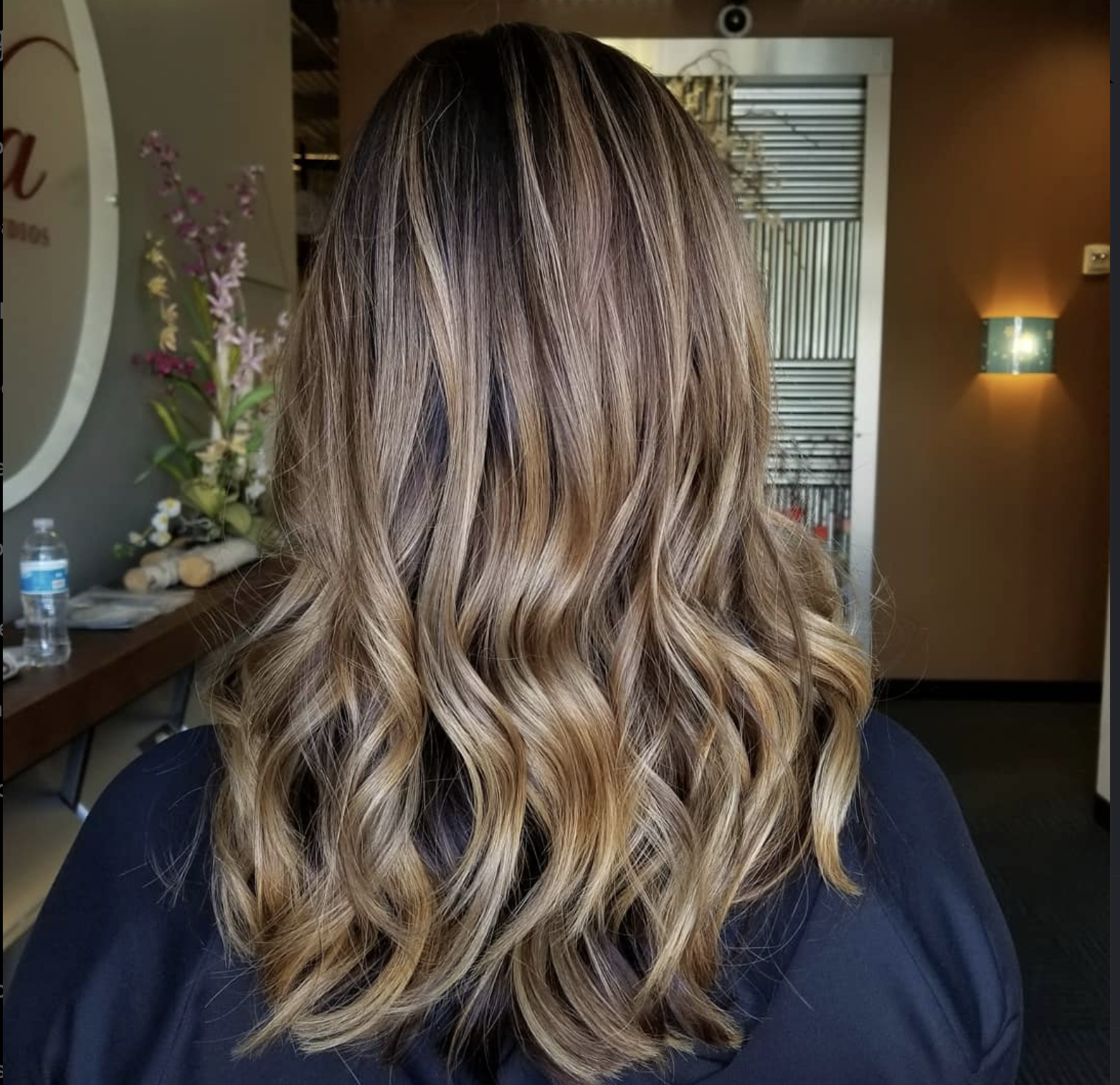 Back view of a woman's shoulder-length hair styled with loose waves and highlights in shades of light brown and blonde.