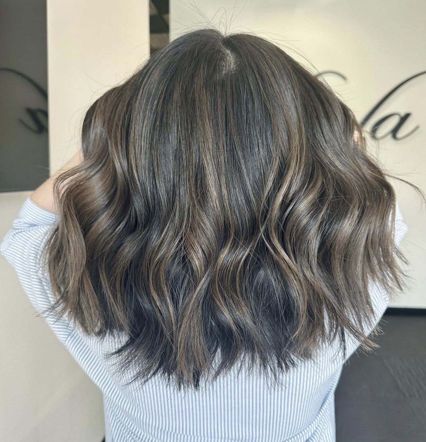 Back view of a person with shoulder-length wavy hair with highlights